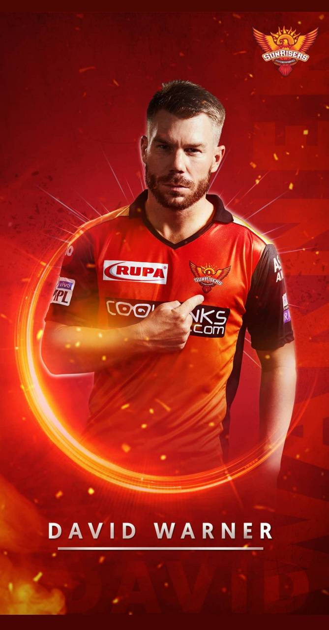 Sunrisers Hyderabad 桌布 壁紙 — 板球運動員大衛·華納身穿橙色球衣，自信地站在火紅背景前，帶有發光的圓形光效。