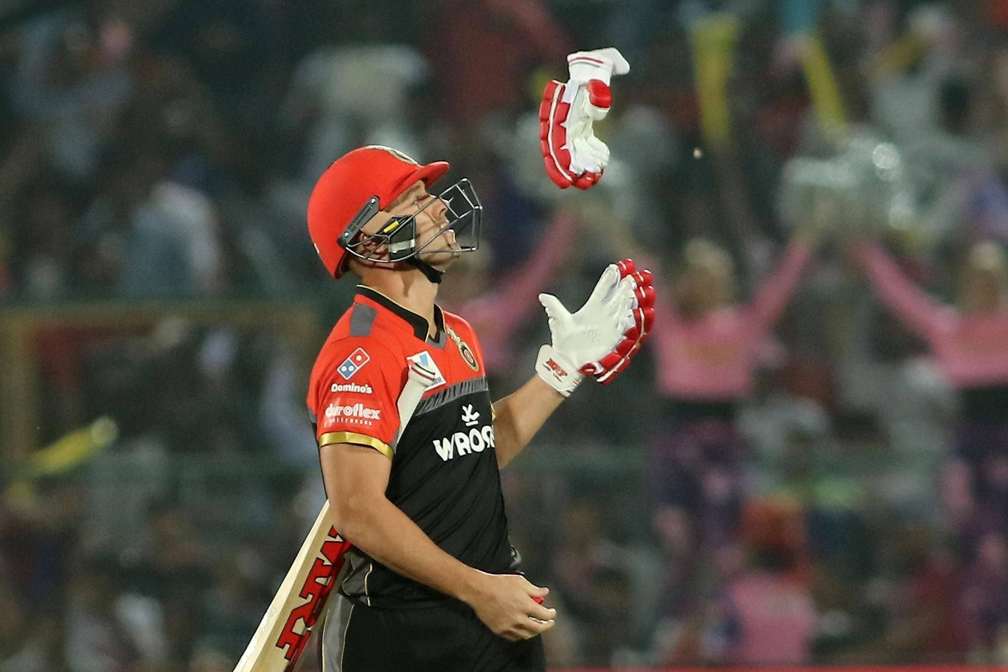 royal challengers bangalore 桌布 壁紙 — 板球運動員戴紅色頭盔、穿黑色球衣，在夜間比賽中手持球棒向上拋白色手套。