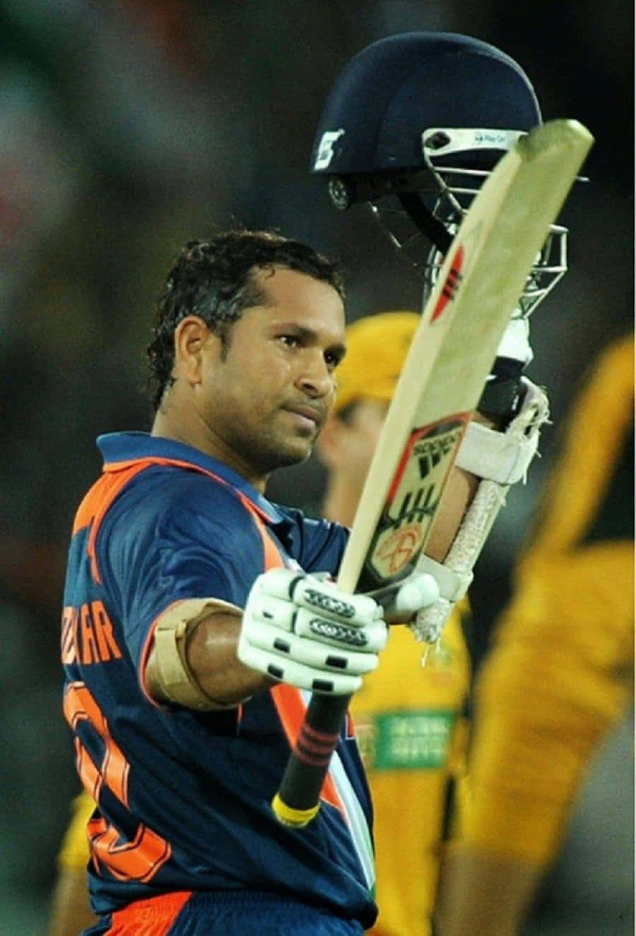 Sachin Tendulkar 桌布 壁紙 — 板球運動員薩欽·坦杜卡在體育場燈光下高舉球棒和頭盔，擺出勝利的姿勢。