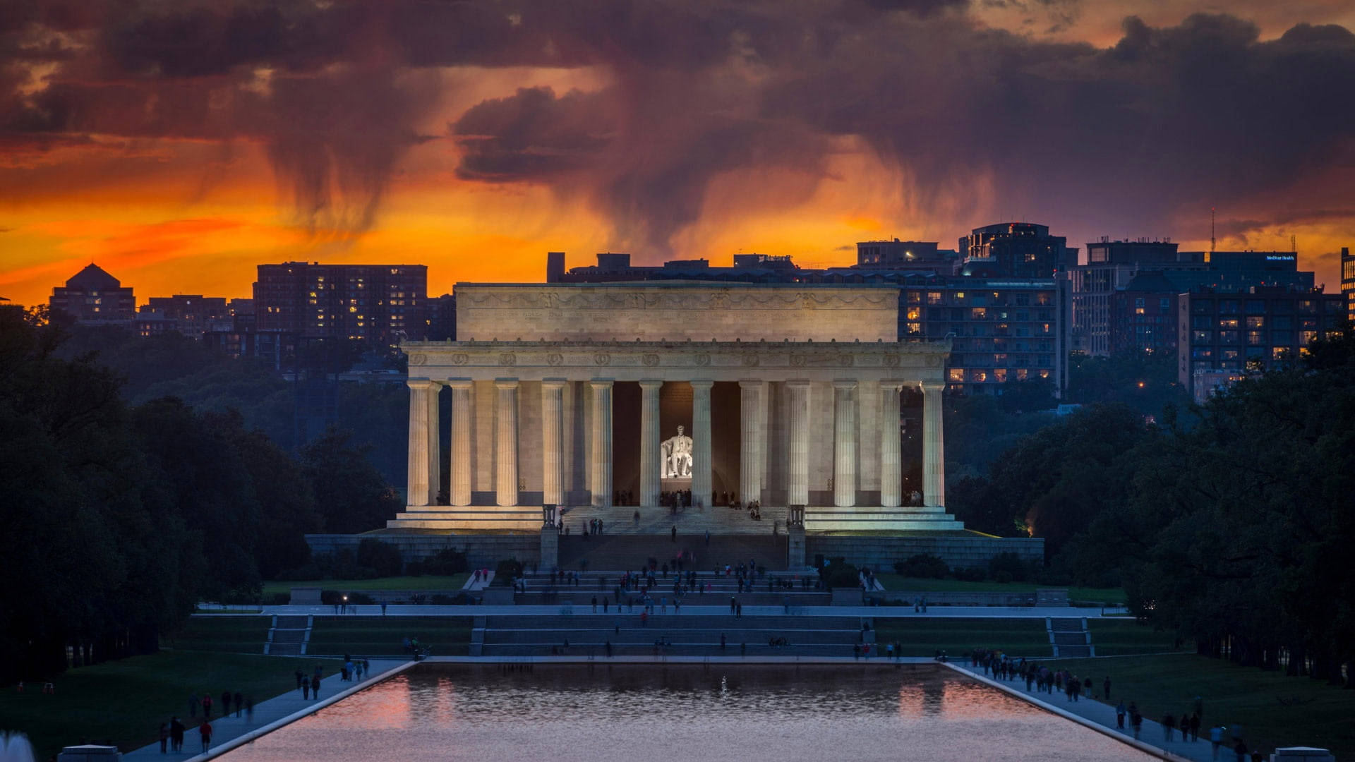 Washington 桌布 壁紙 — 林肯紀念堂在日落時分被照亮，戲劇性的橙色雲彩和城市燈光倒映在倒影池中。