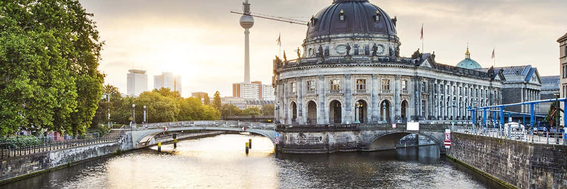 Berlin 桌布 壁紙 — 柏林國會大廈倒映在施普雷河上，金色的夕陽照耀著歷史建築和周圍的樹木。
