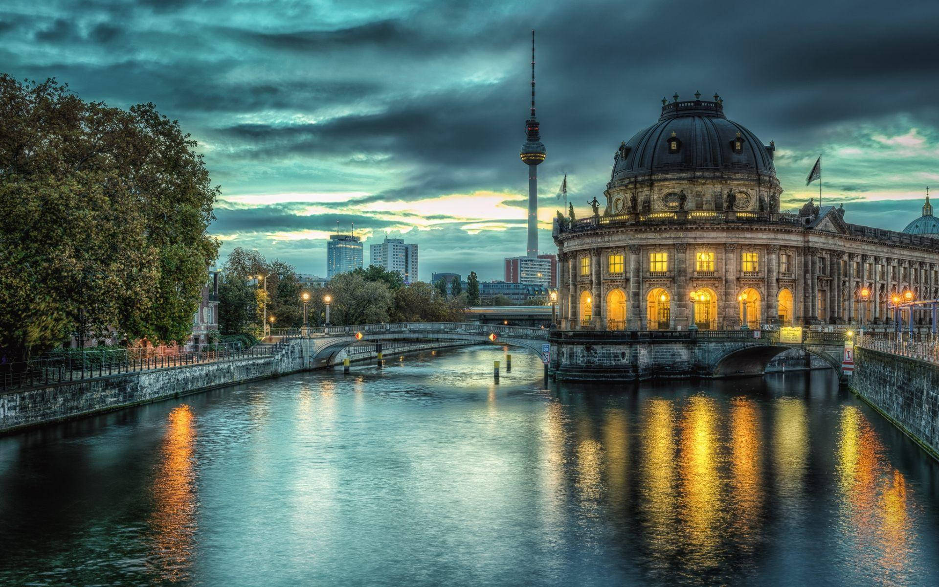 Berlin 桌布 壁紙 — 柏林國會大廈在憂鬱的暮色天空下溫暖地發光，燈光倒映在平靜的施普雷河上。