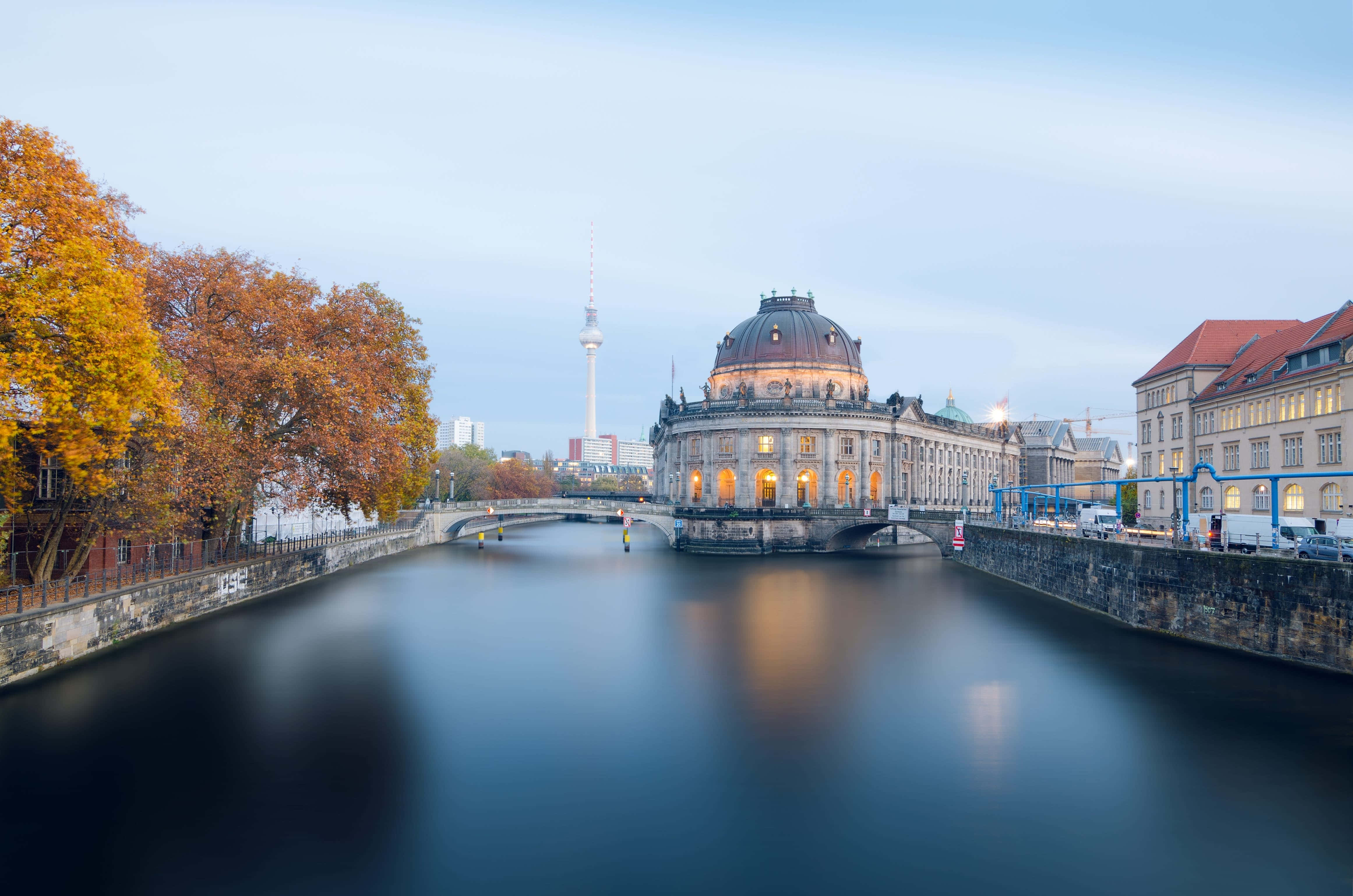 Berlin 桌布 壁紙 — 柏林國會大廈在黃昏時溫暖地發光，倒映在兩旁種滿秋樹的平靜河流中。