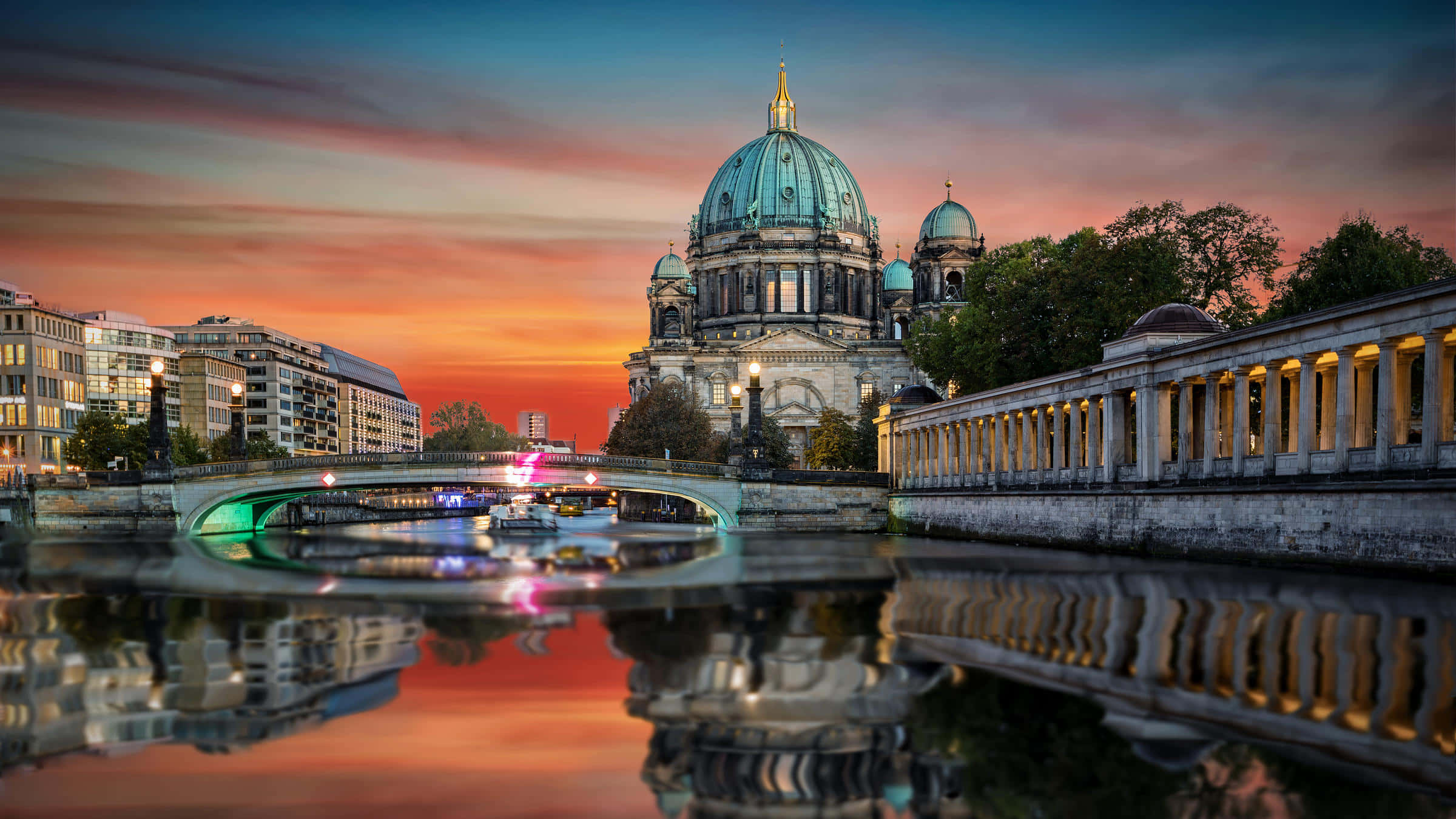 Berlin 桌布 壁紙 — 柏林大教堂倒映在施普雷河上，天空呈現 vibrant 的日落色彩，帶有條紋雲彩和閃爍的城市燈光。