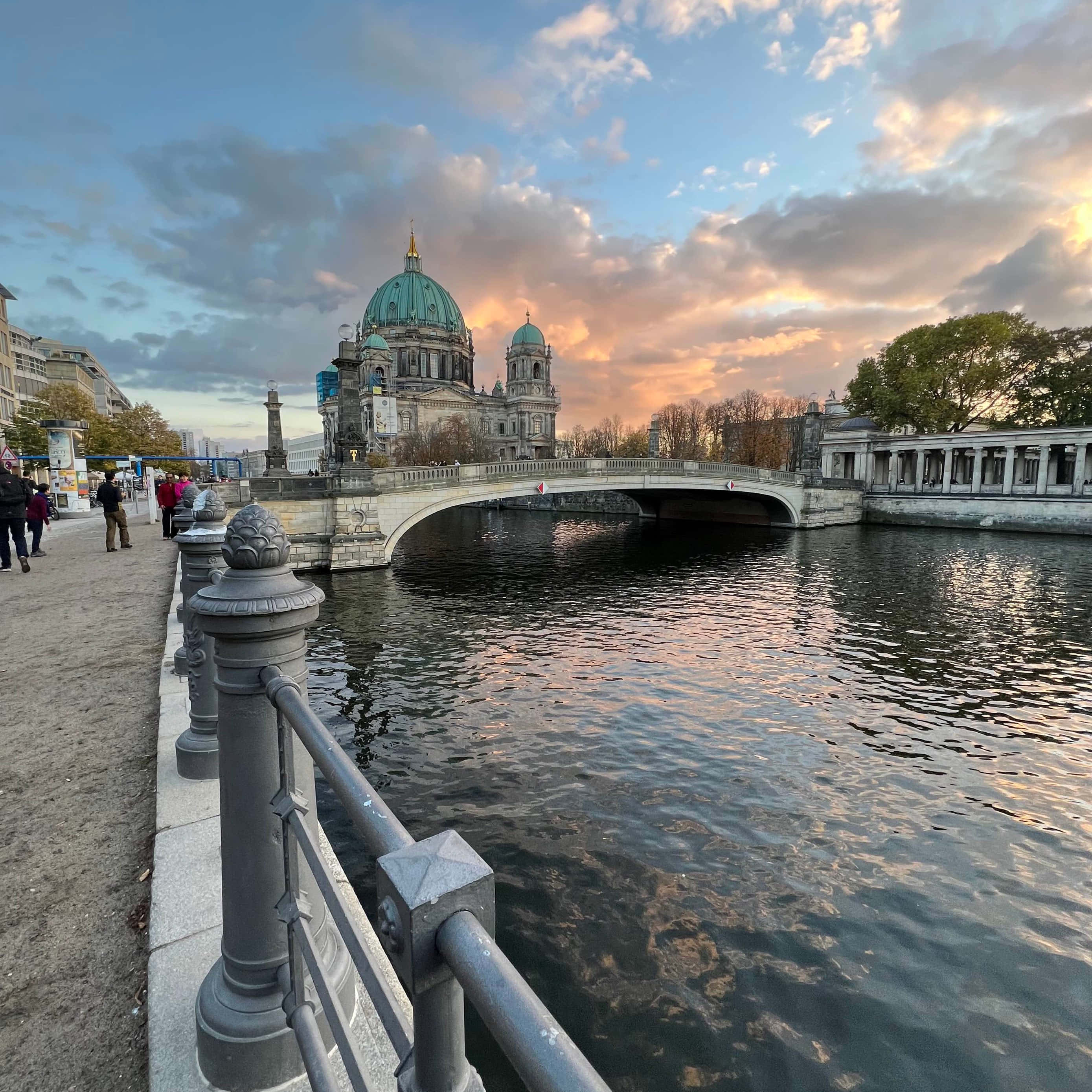 Berlin 桌布 壁紙 — 柏林大教堂在日落時分雄偉地矗立在一條河流上的橋對面，金色的雲彩倒映在水面上。