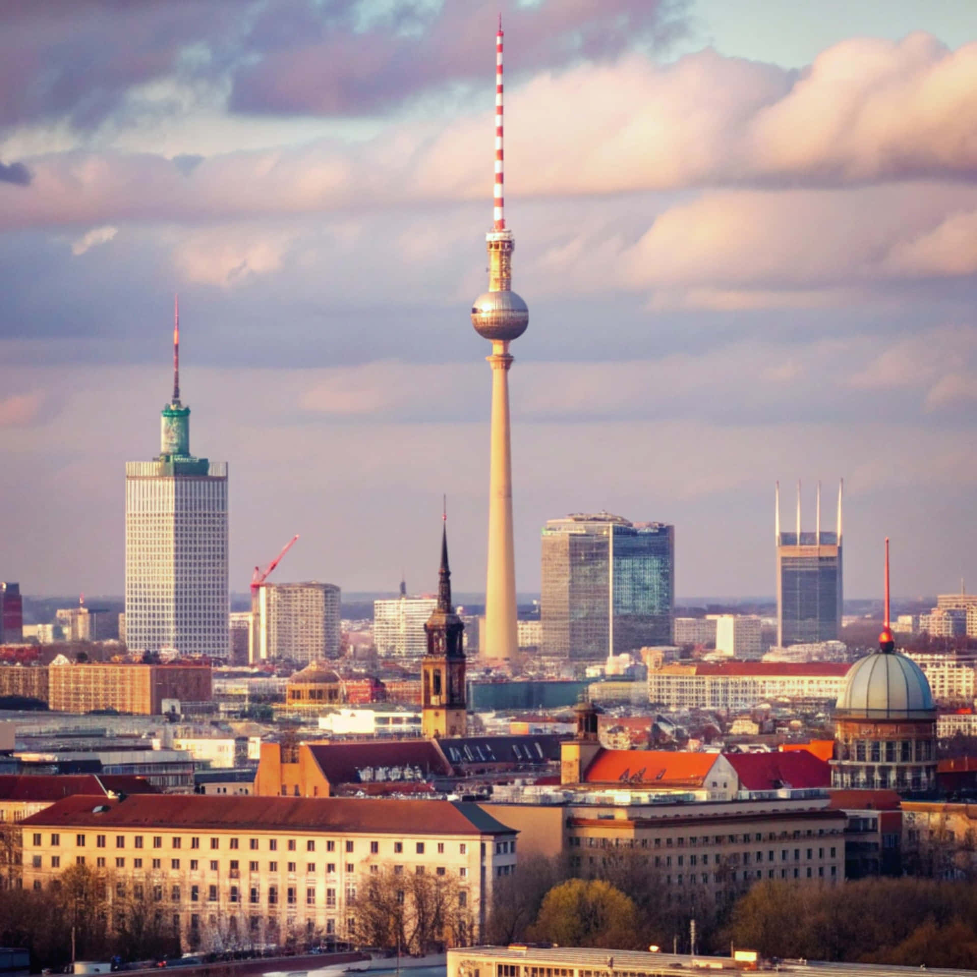 Berlin Skyline 壁紙 — 柏林天際線在黃昏時分，標誌性的電視塔和現代摩天大樓在柔和的粉紅色和灰色雲層下聳立於歷史屋頂之上。