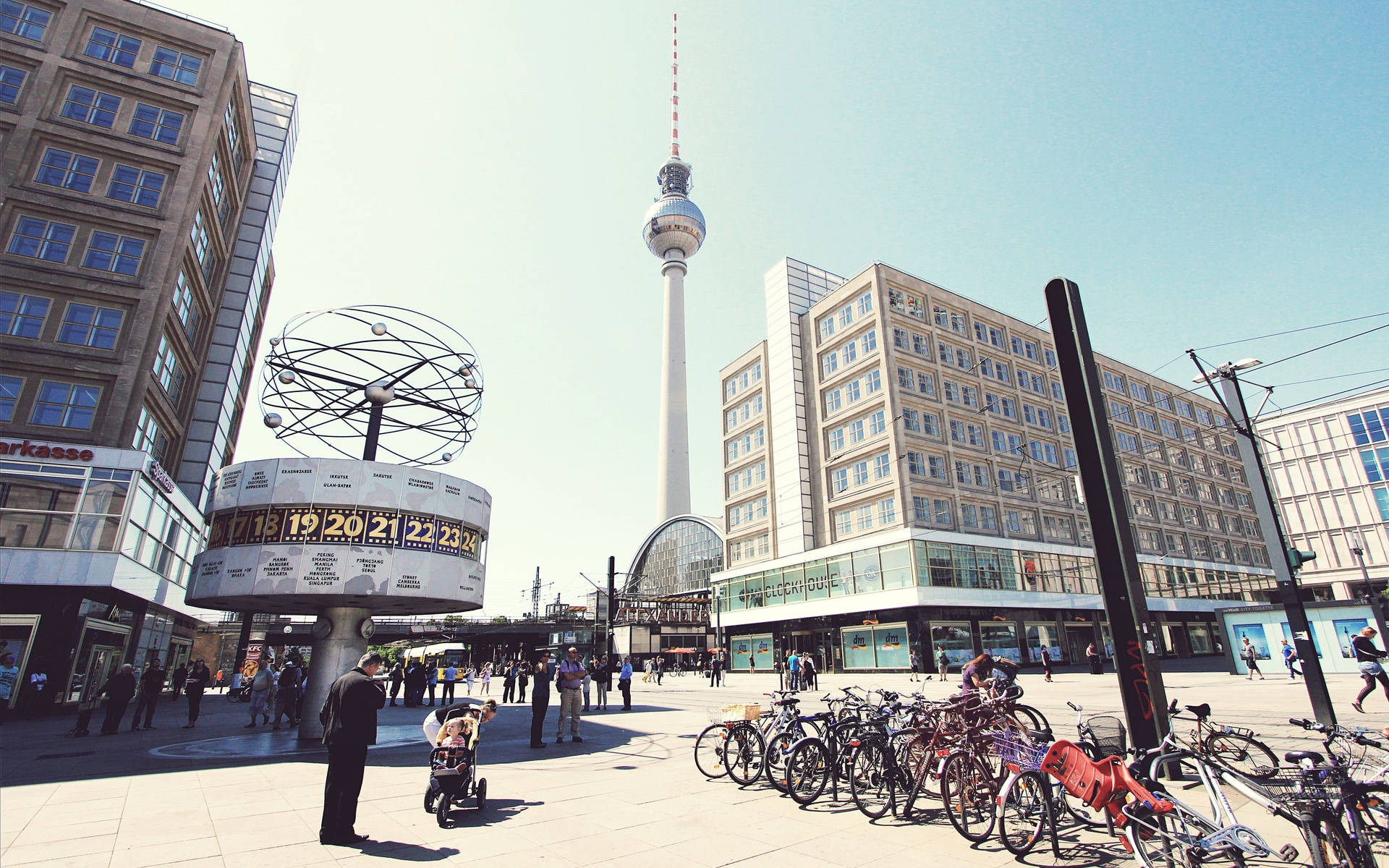 Berlin 桌布 壁紙 — 柏林標誌性的電視塔聳立在陽光明媚的城市廣場上，廣場上充滿了自行車和行人，靠近原子球雕塑。