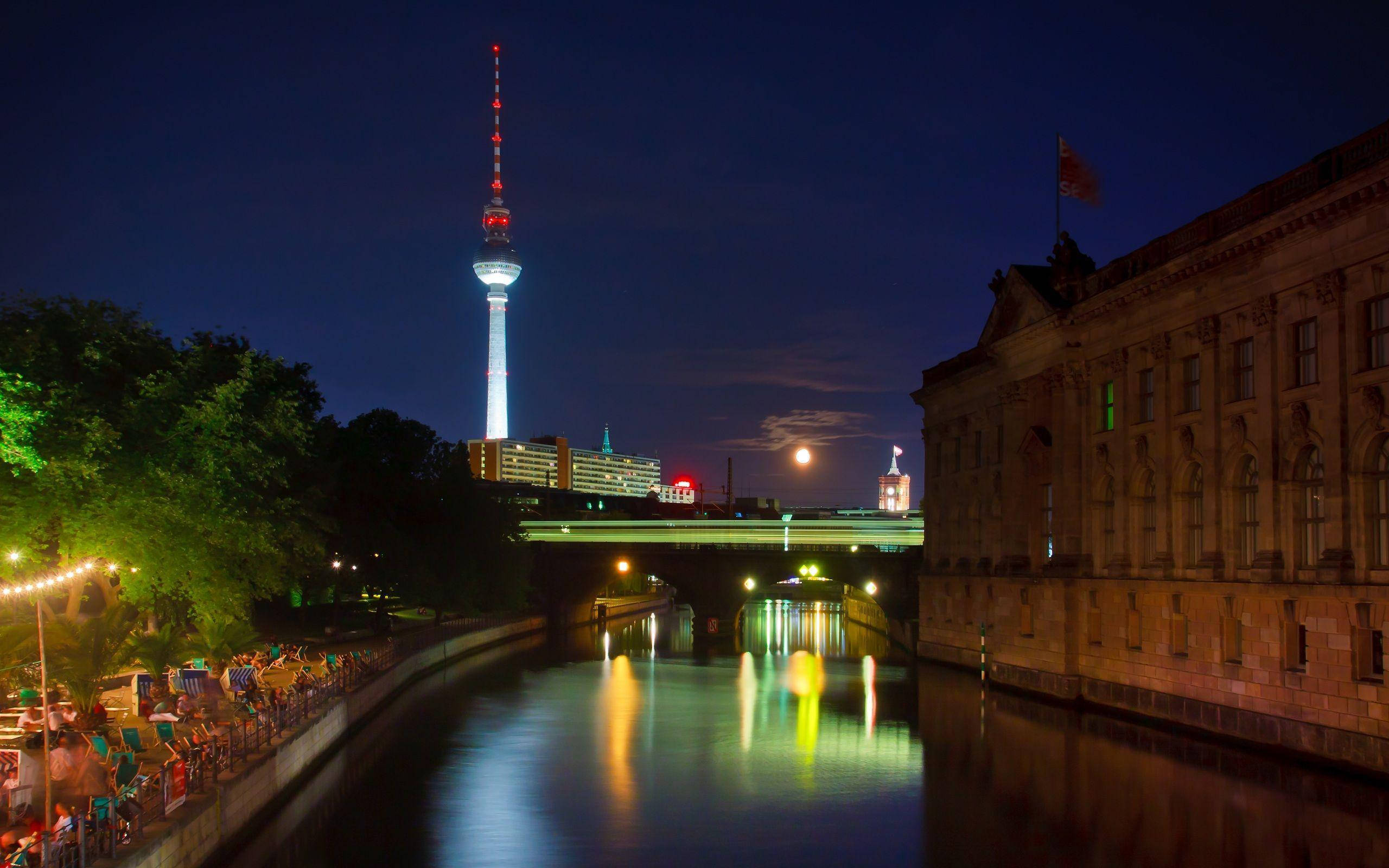 Berlin 桌布 壁紙 — 柏林電視塔在夜晚發光，映照在河面上，反射城市燈光和滿月。