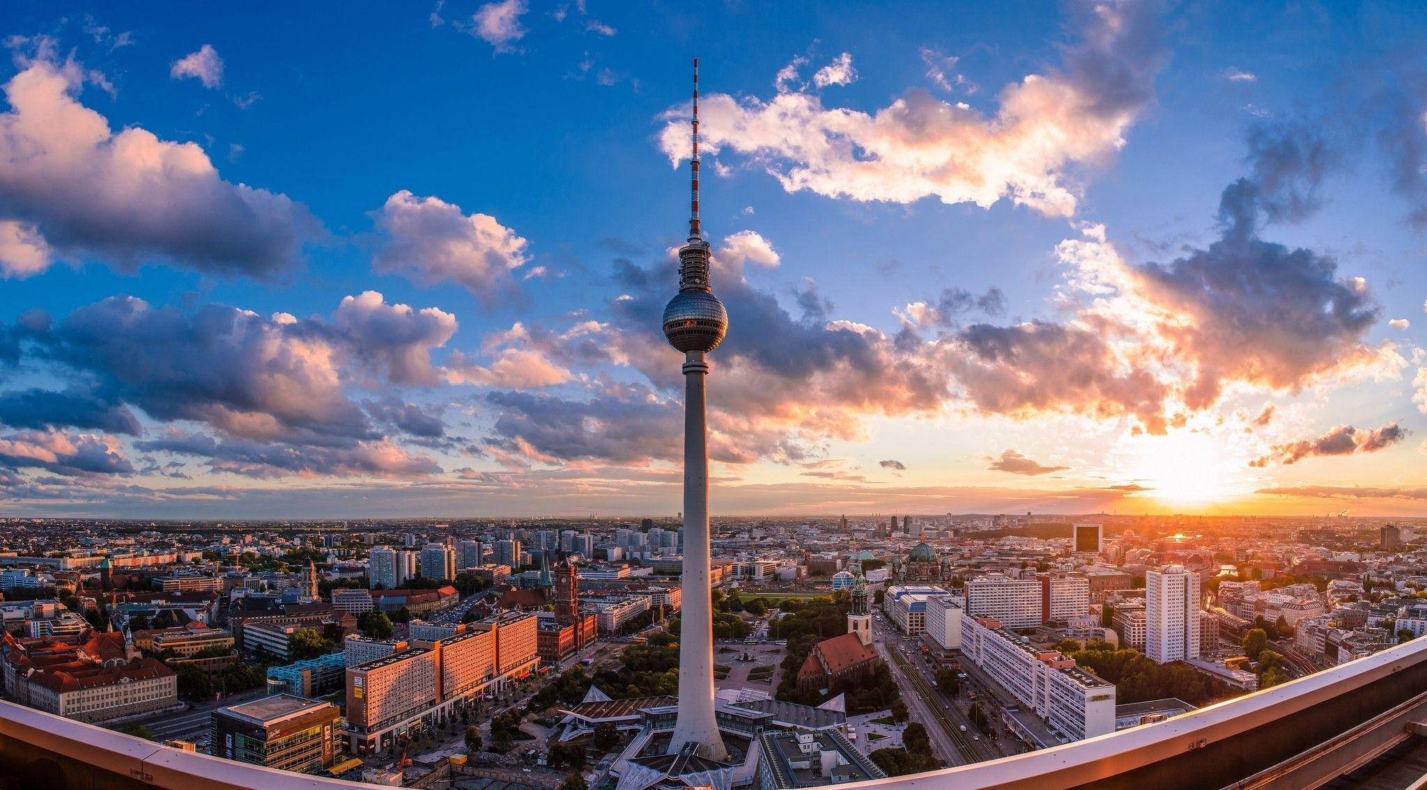 Berlin 桌布 壁紙 — 柏林電視塔在戲劇性的日落天空下高聳，金色雲彩覆蓋著廣闊的城市景觀。