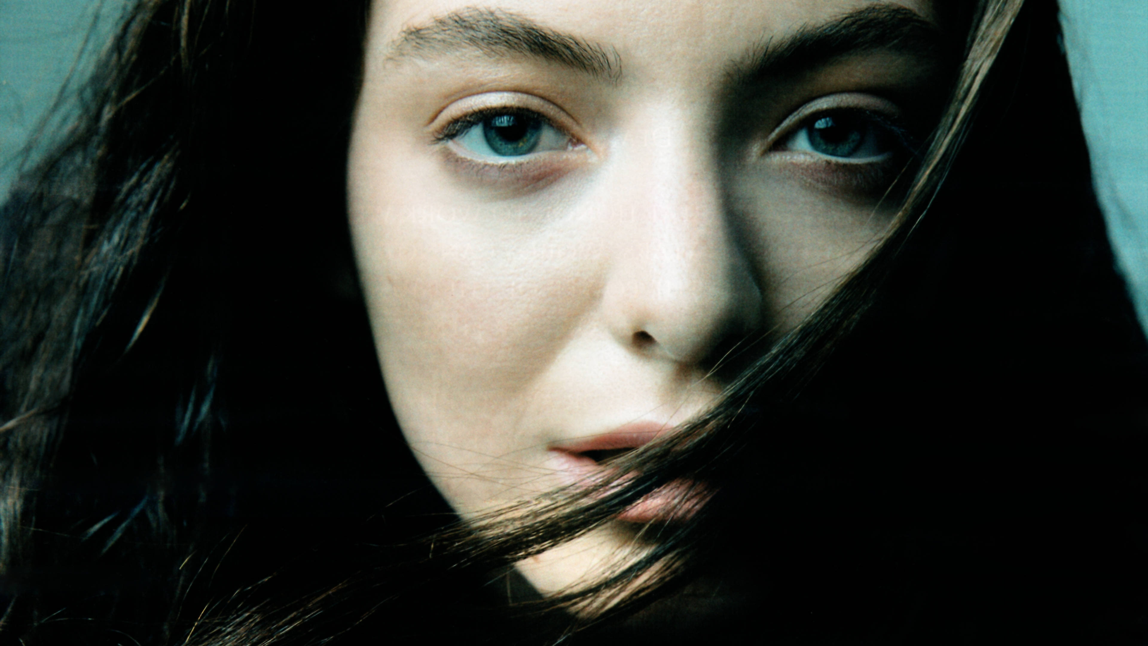 Lorde 桌布 壁紙 — 柔光下，一名女子近距離肖像，擁有引人注目的藍色眼睛和部分遮蓋臉龐的深色頭髮。