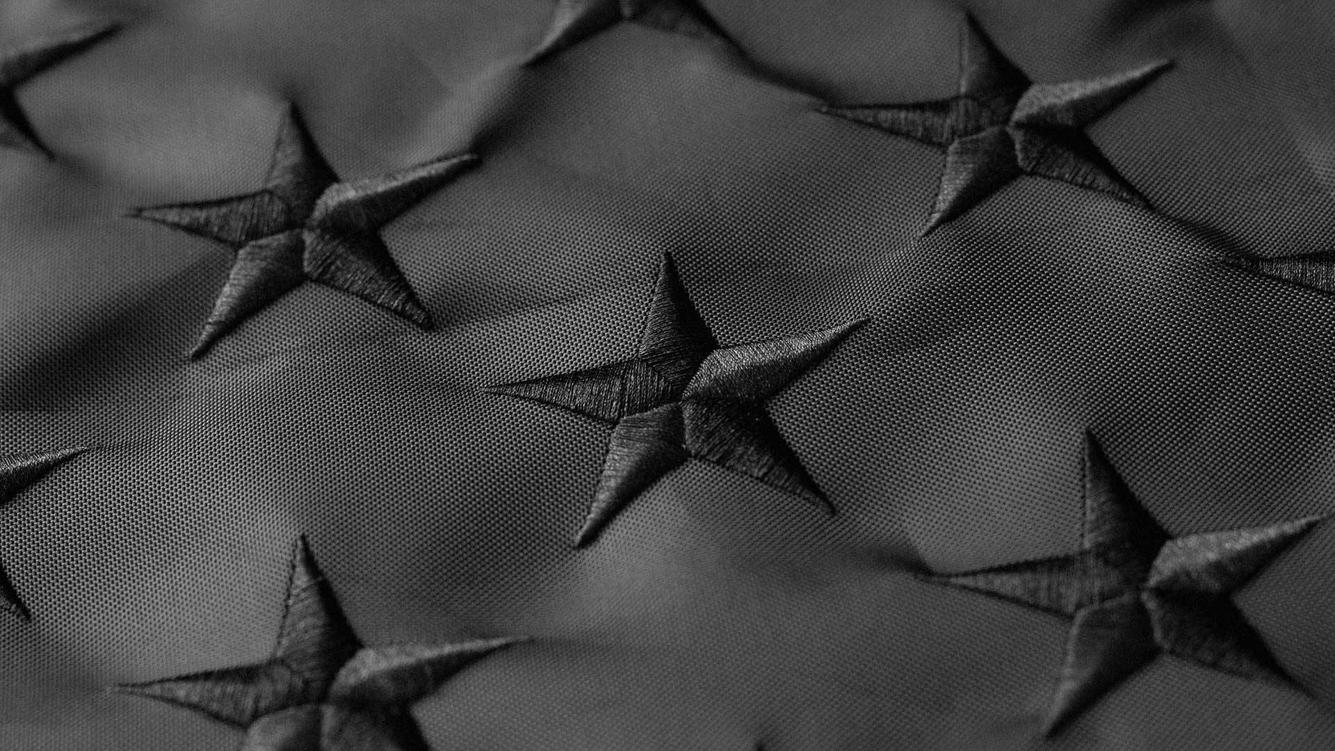 Black American Flag 桌布 壁紙 — 柔光下帶有凸起星星圖案的紋理黑色織物特寫。