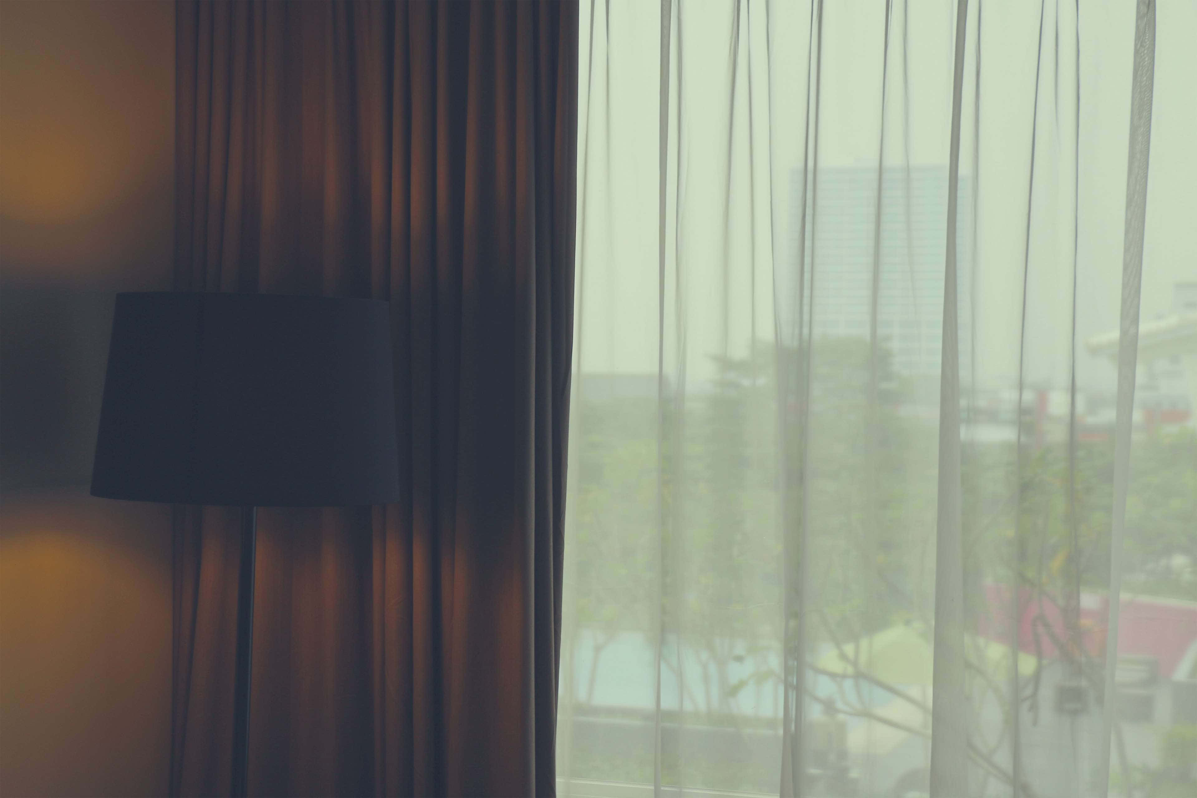 Hotel Room 桌布 壁紙 — 柔和光線穿過薄紗窗簾，顯露出暗色燈旁窗外的朦朧城市景觀。