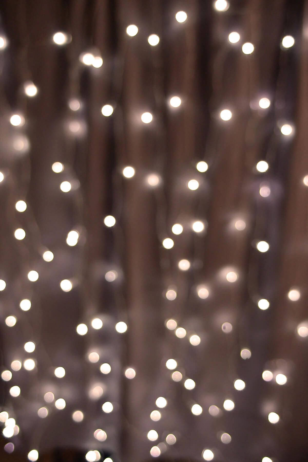 Christmas Lights Aesthetic 桌布 壁紙 — 柔和散景效果，發光的白色童話燈垂直懸掛在深色窗簾背景上。