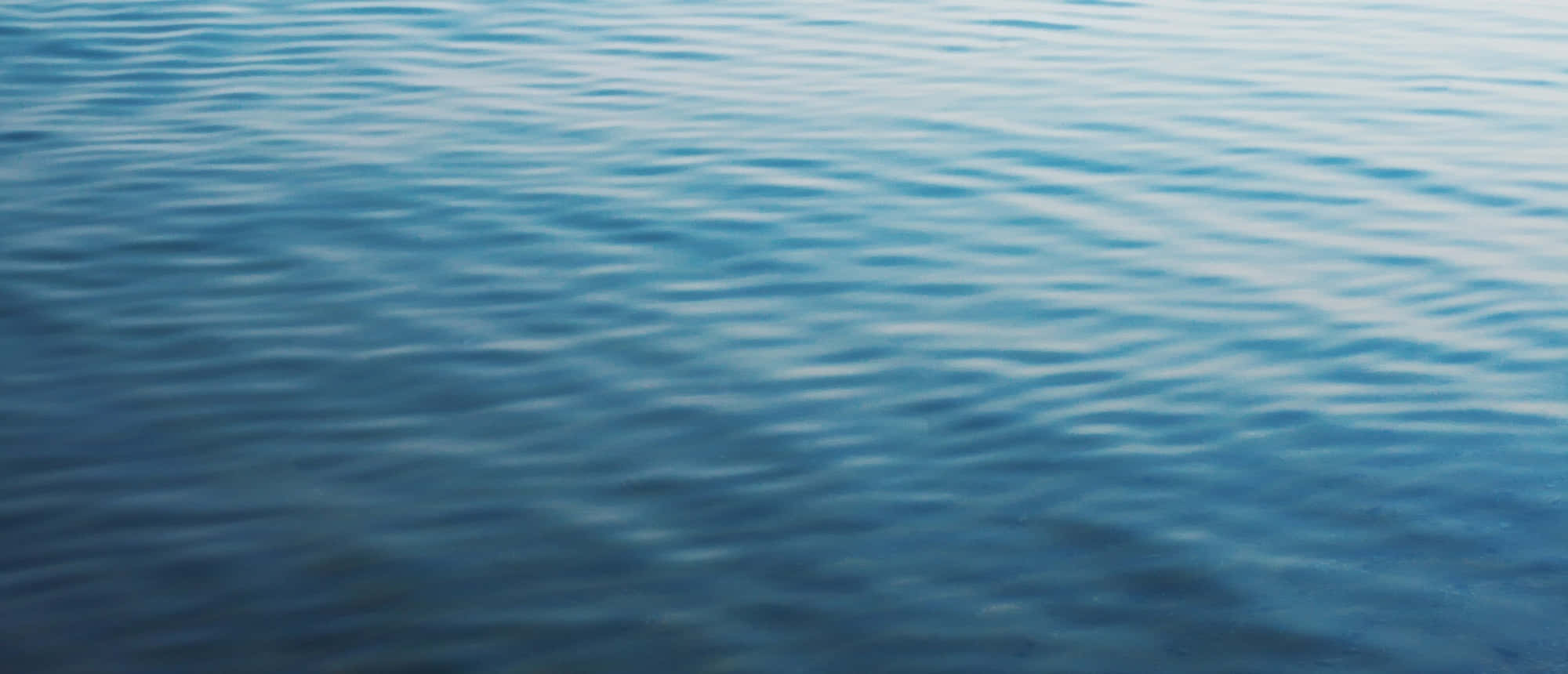 Ocean Water 桌布 壁紙 — 柔和日光下，平靜的藍色水波紋營造出寧靜的自然質感。