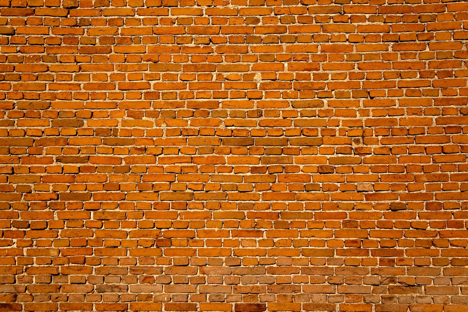 Brick 桌布 壁紙 — 柔和日光下，風化磚牆的近距離特寫，帶有溫暖的橙色色調和可見的砂漿線。