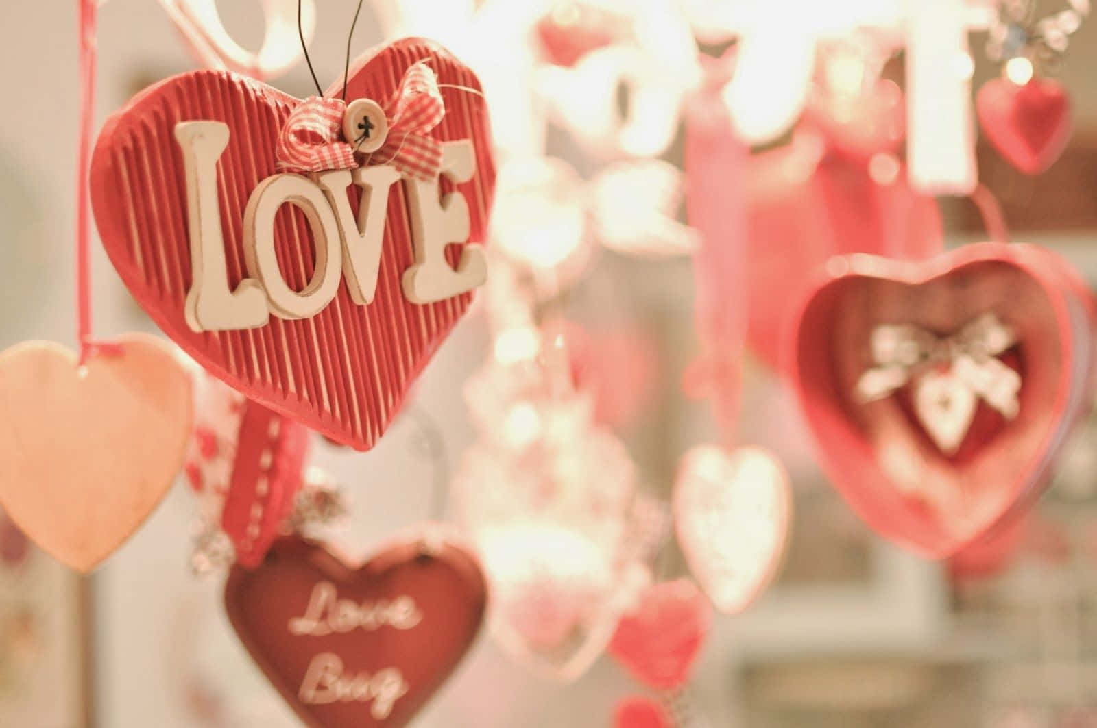 愛心 桌布 壁紙 — 柔和焦點的懸掛紅色木心，上面有 'LOVE' 和 'Love Bug' 字樣，並飾有蝴蝶結。