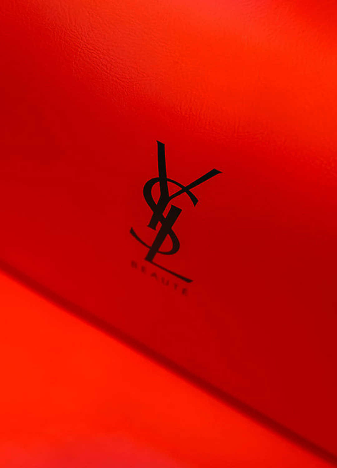 YSL 桌布 壁紙 — 柔和燈光下，在質感豐富的紅色表面上特寫一個大膽的黑色YSL Beauté標誌。