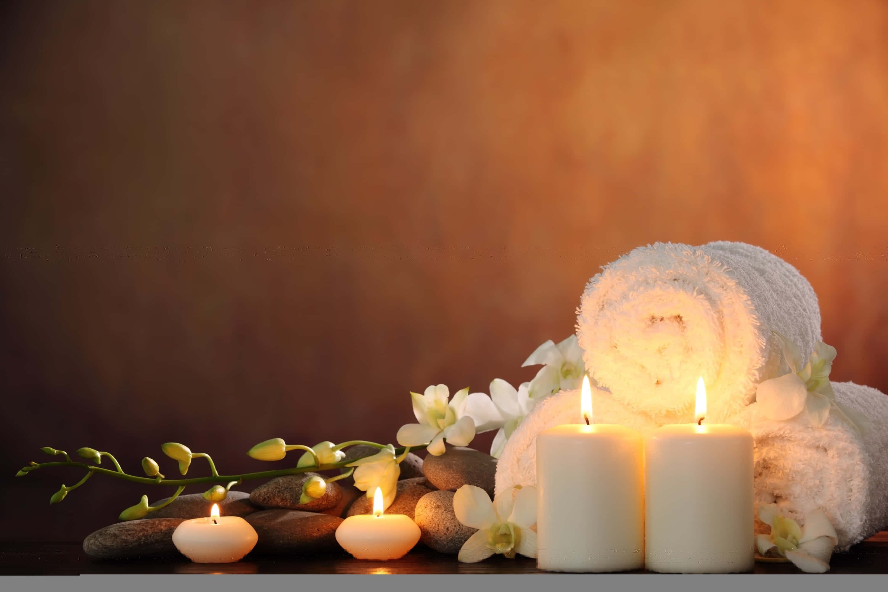 Spa Treatments 桌布 壁紙 — 柔和燈光的SPA場景，白色毛巾捲、蠟燭和蘭花排列在光滑的石頭上，背景為溫暖的漸變色。