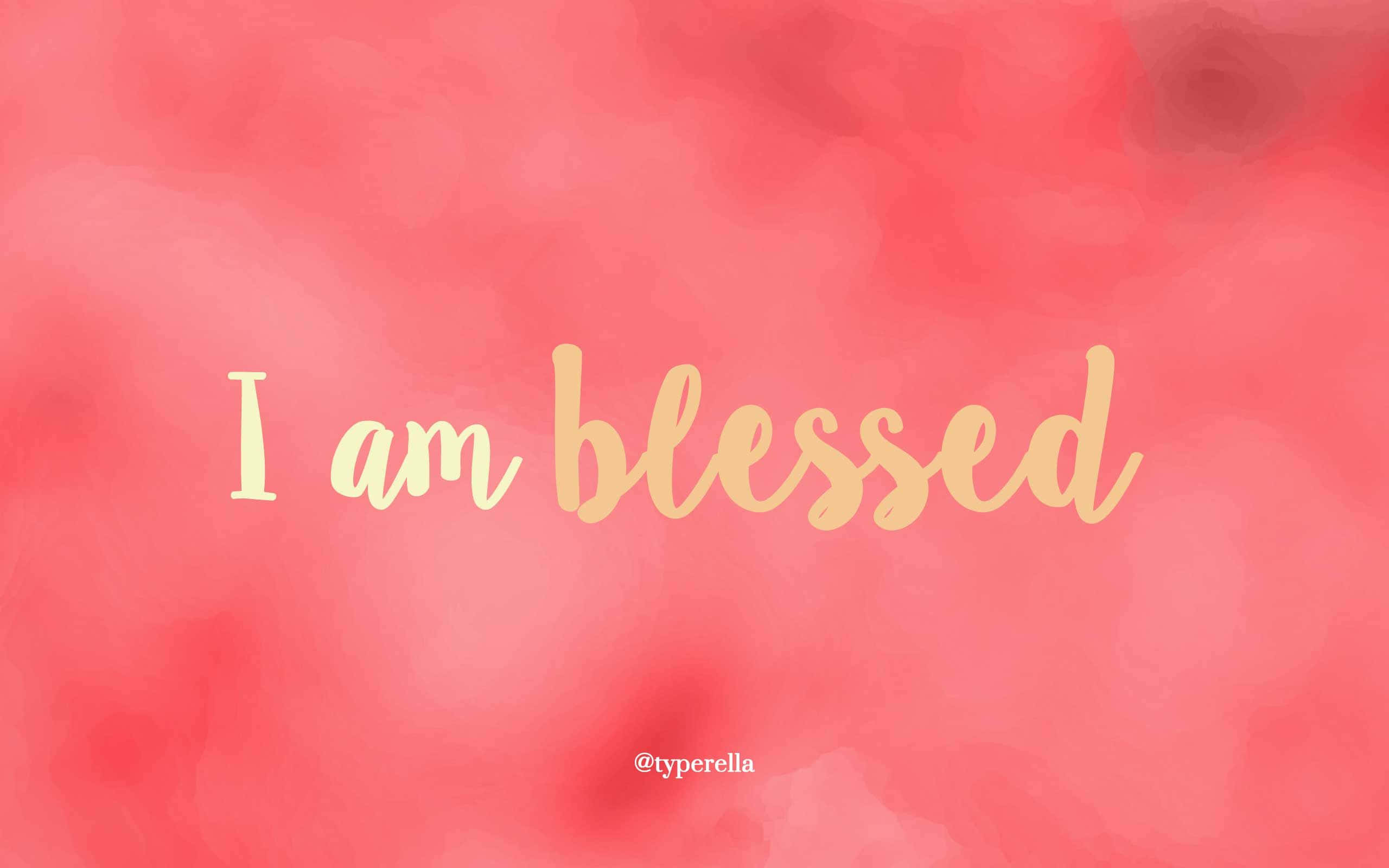 桌布 壁紙 — 柔和珊瑚色水彩背景，金色草書文字寫著「I am blessed」，並附有小型版權浮水印。