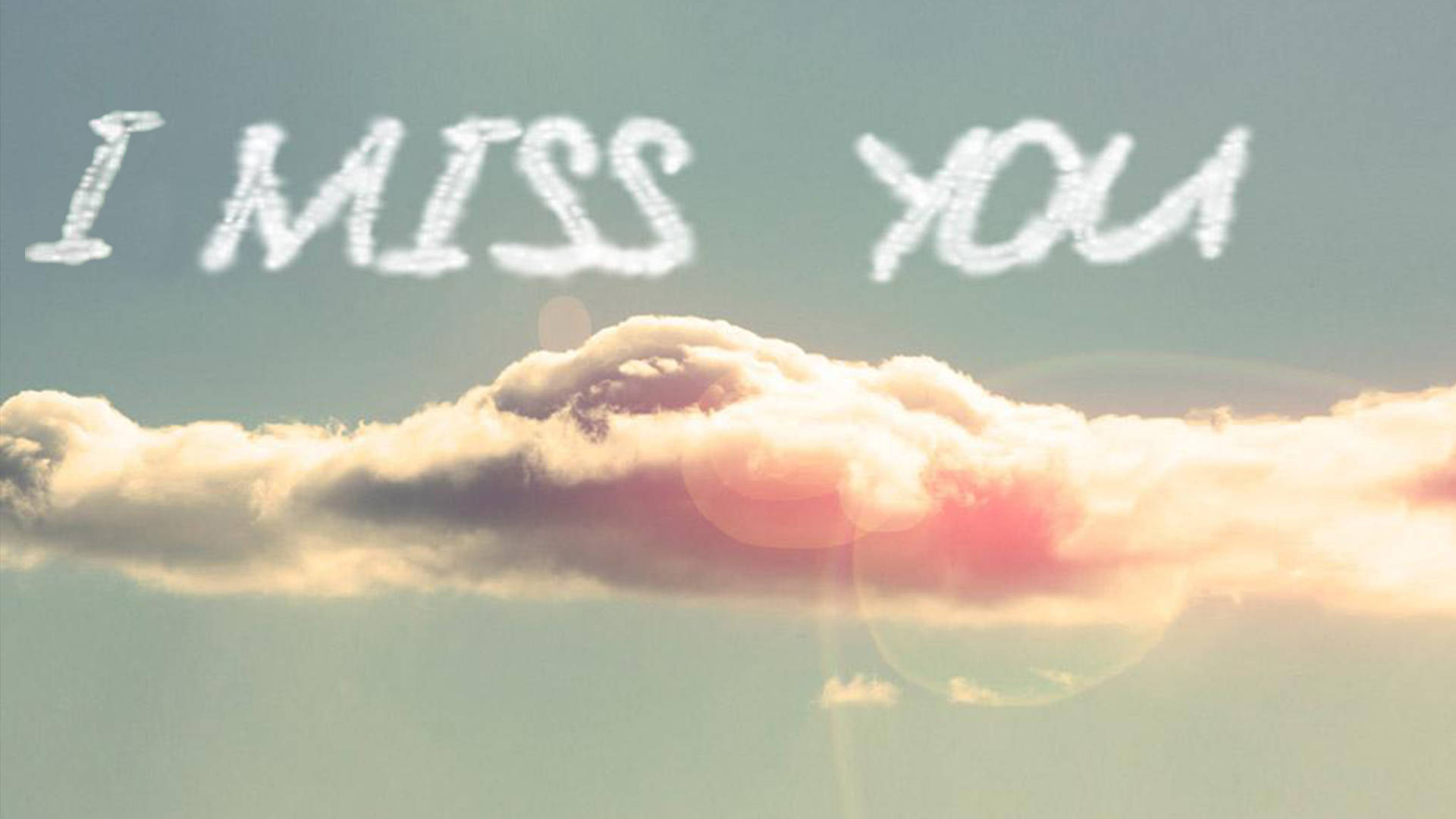 I Miss You 桌布 壁紙 — 柔和的天空中，雲朵形成「I MISS YOU」的字樣，帶有溫暖的日落光芒和鏡頭光暈。