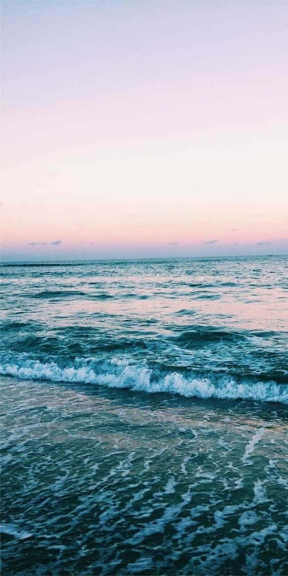 Cute Sea 桌布 壁紙 — 柔和的海浪在粉彩粉紅和薰衣草色的日落天空下拍打著海岸。