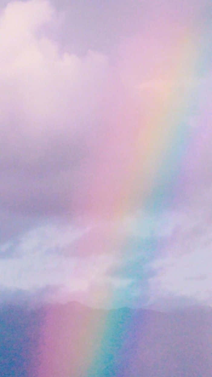 Cute Rainbow 桌布 壁紙 — 柔和的粉彩彩虹穿過夢幻的薰衣草雲層，在薄霧籠罩的山巒之上，寧靜的天空中形成一道弧線。