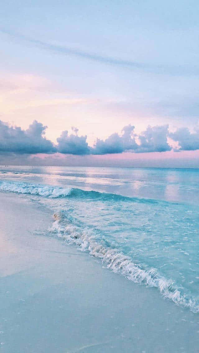 Pastel Beach 桌布 壁紙 — 柔和的粉彩波浪在夢幻般的暮色天空下，伴隨著粉紅色和藍色的雲朵，輕輕地拍打著寧靜的海灘。