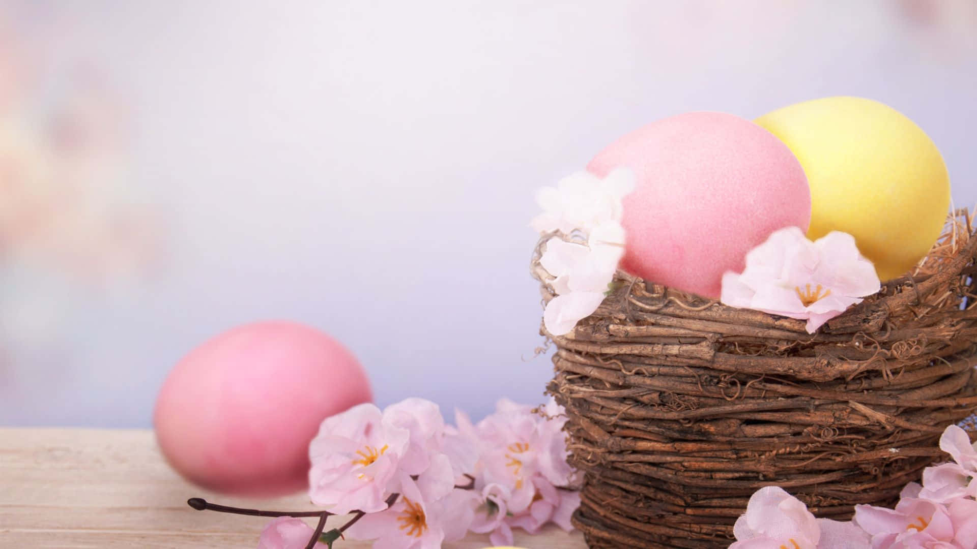 Easter Egg 桌布 壁紙 — 柔和的粉彩蛋放在編織籃中，配以櫻花，置於木質表面上。