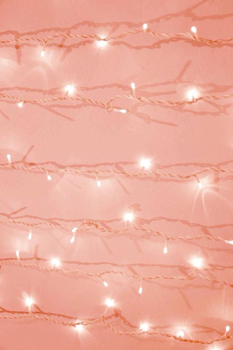 Christmas Lights iPhone 桌布 壁紙 — 柔和的粉紅色串燈在帶有紋理的牆壁上溫暖地發光，在舒適的氛圍中投下柔和的陰影。