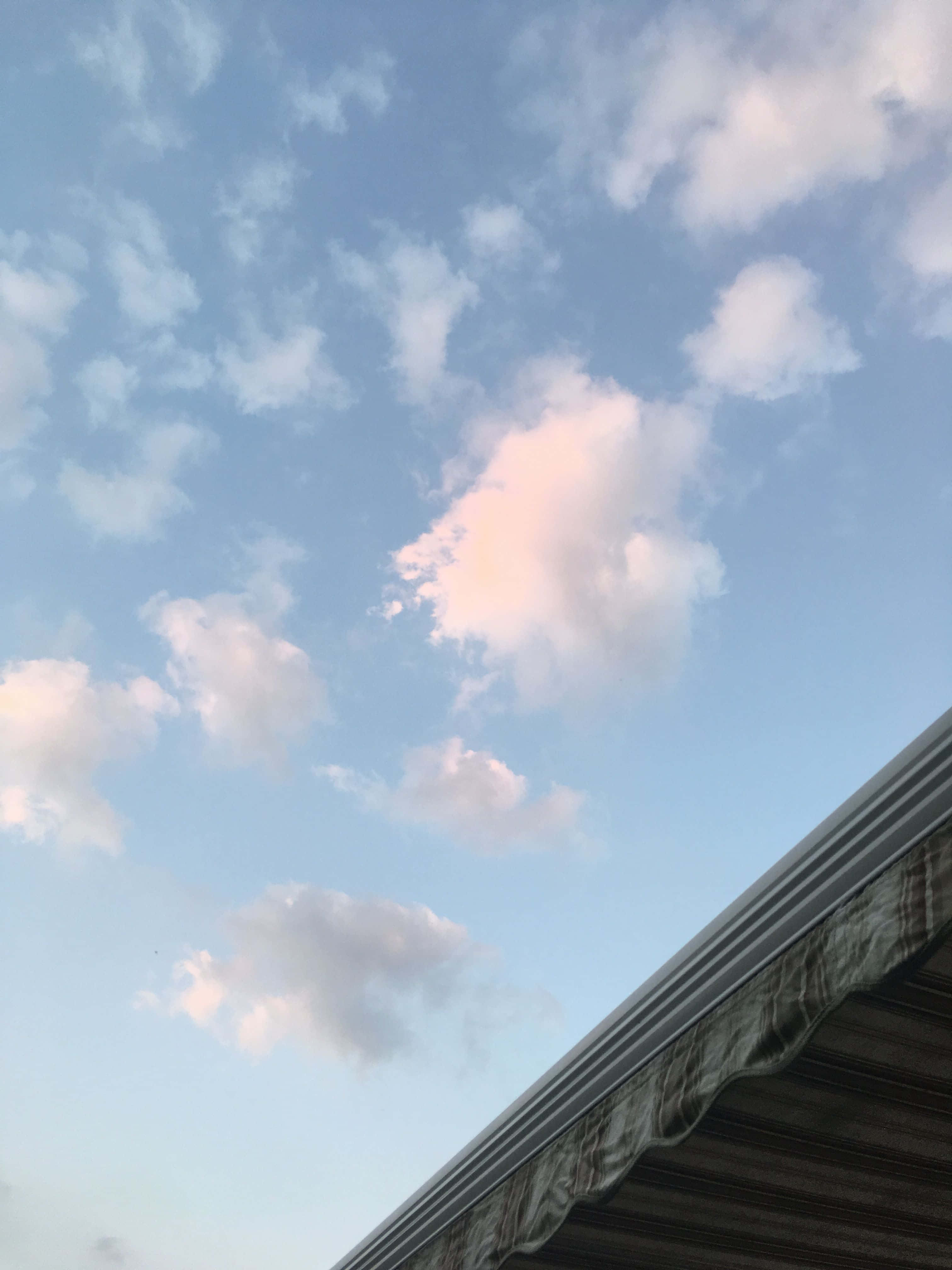 Aesthetic Sky 桌布 壁紙 — 柔和的粉紅色和白色雲朵在黃昏時分飄過圖案遮陽篷上方的淡藍色天空。