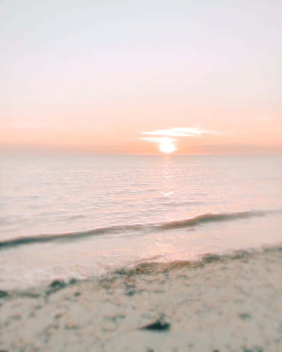 Beach Aesthetic 桌布 壁紙 — 柔和的粉紅色日落照耀著平靜的海水與沙灘交匯處，呈現輕柔的模糊效果。