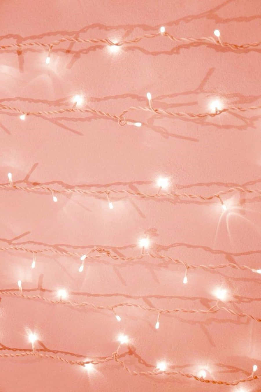 Peach Aesthetic 桌布 壁紙 — 柔和的粉紅色燈串在相配的粉彩牆前溫暖地發光，營造出舒適的室內環境。
