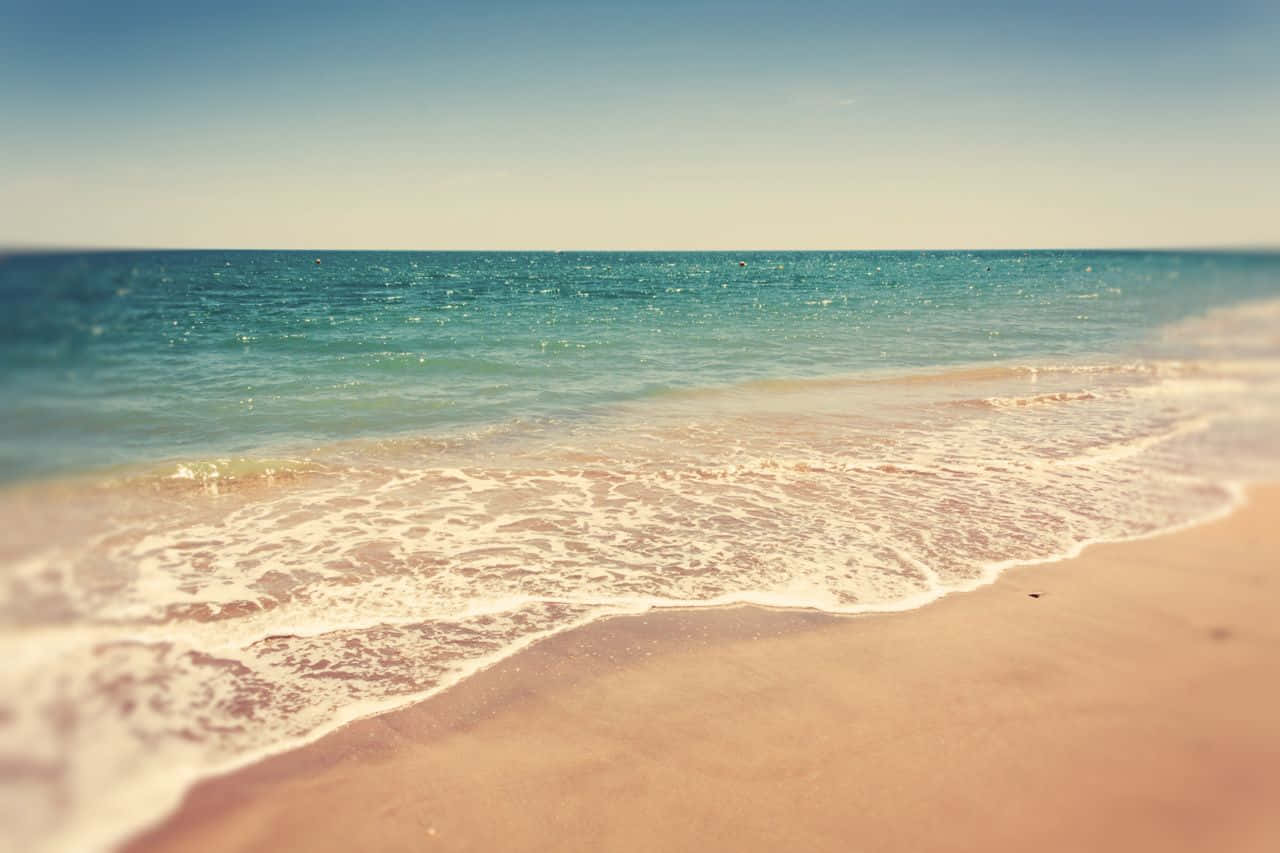 Sea Aesthetic 桌布 壁紙 — 柔和的藍綠色海浪輕輕拍打溫暖的粉紅色沙灘，在晴朗的藍天下。