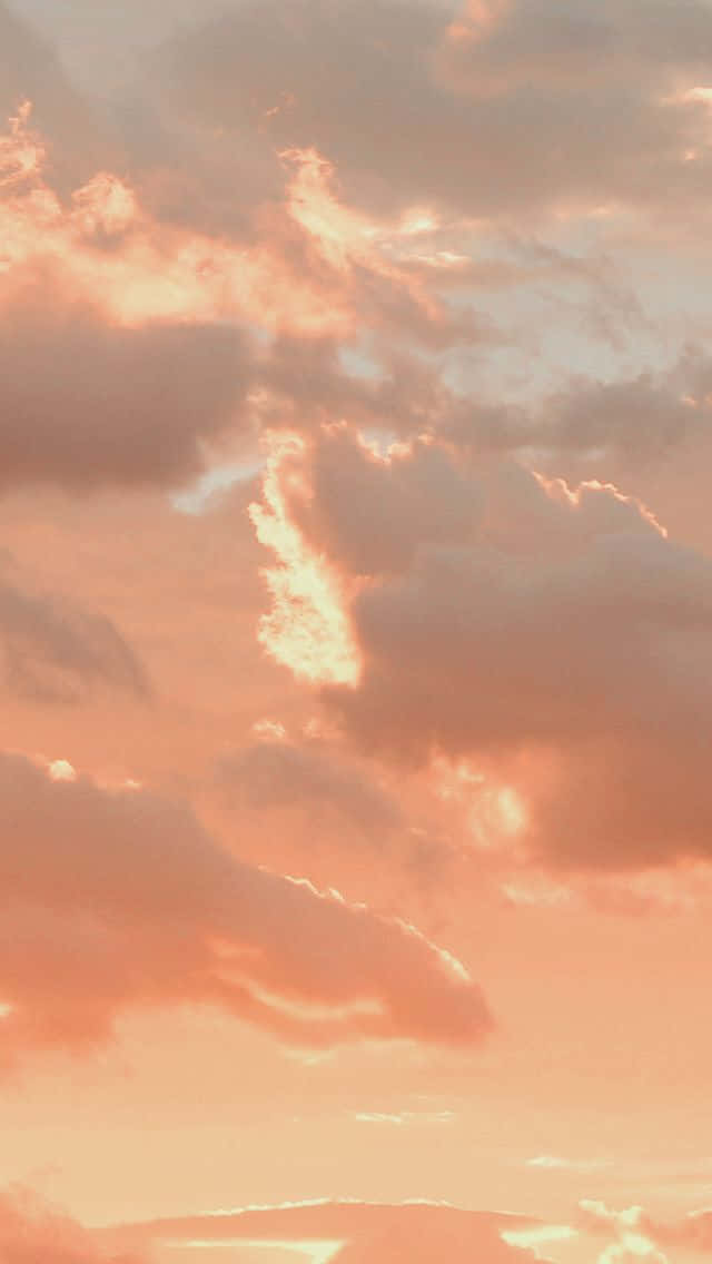 美學雲朵 桌布 壁紙 — 柔和的蜜桃色和粉紅色雲朵在昏暗的天空中溫暖地發光，微妙的陽光穿透雲層。