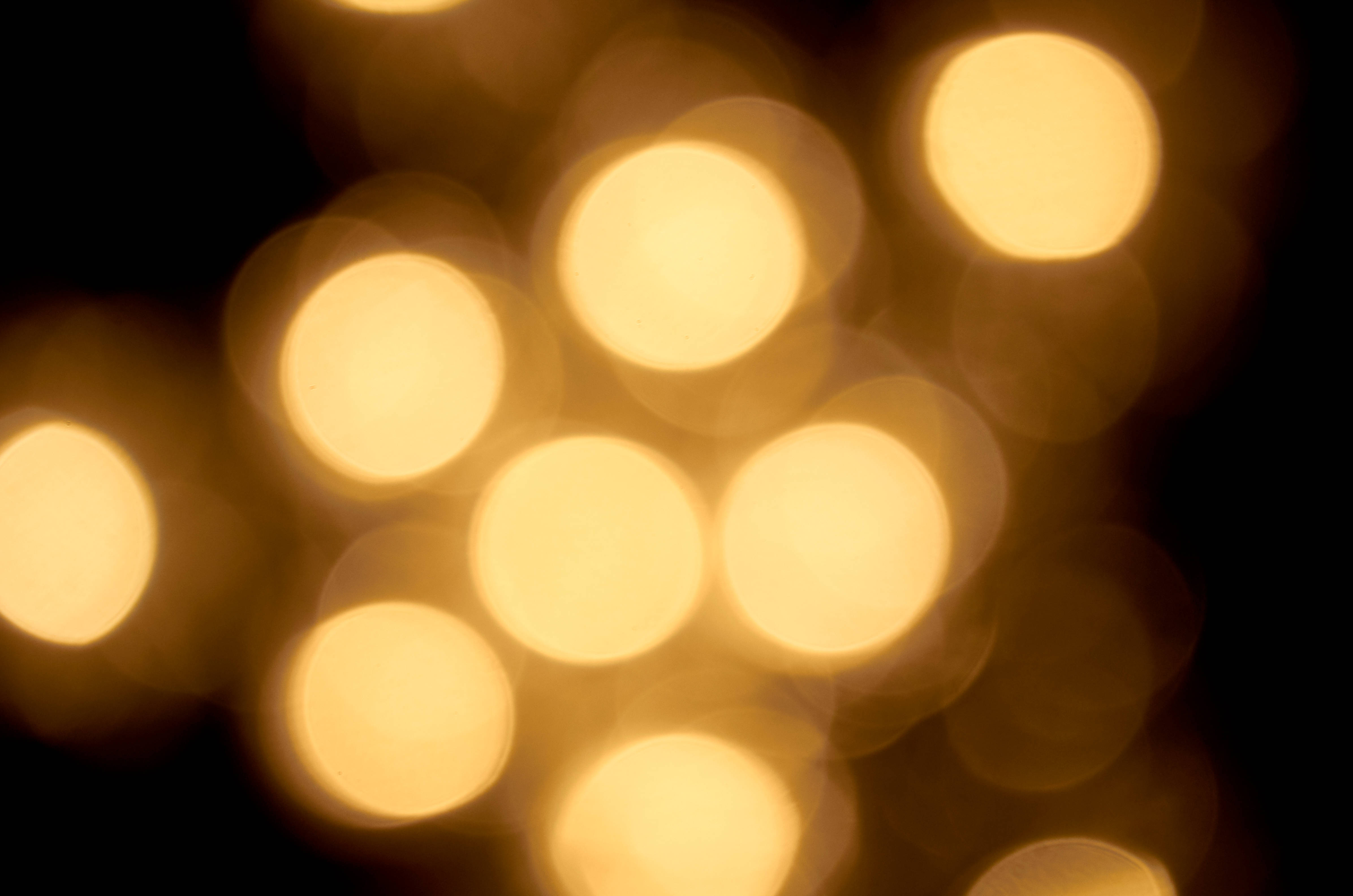 Bokeh 桌布 壁紙 — 柔和的金色散景燈光在深黑色背景上溫暖地發光，營造出夢幻般的抽象氛圍。