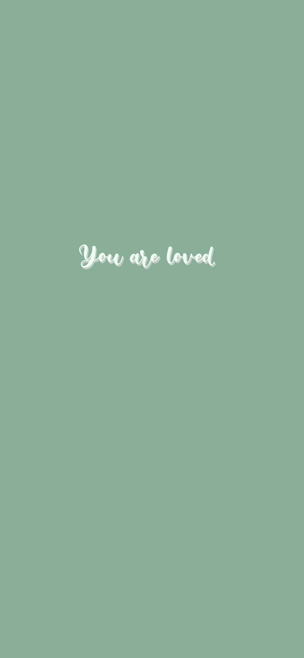 綠色美學 桌布 壁紙 — 柔和的鼠尾草綠色背景，中央以優雅的白色草書顯示「你被愛著」這句話。