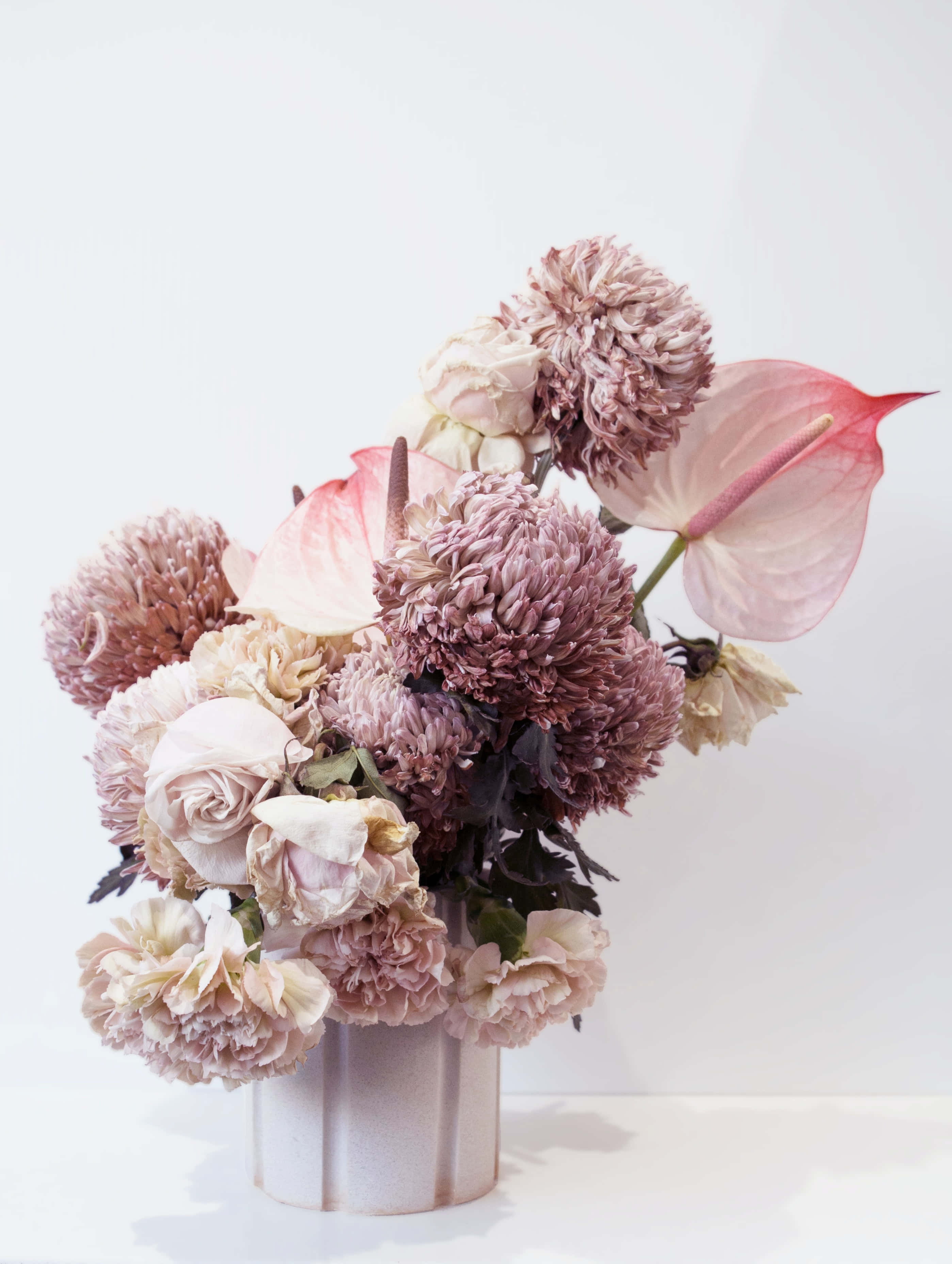 Floral Arrangement 桌布 壁紙 — 柔和粉彩花卉佈置，包括玫瑰、菊花和火鶴花，置於有紋理的花瓶中，以簡約白色背景襯托。