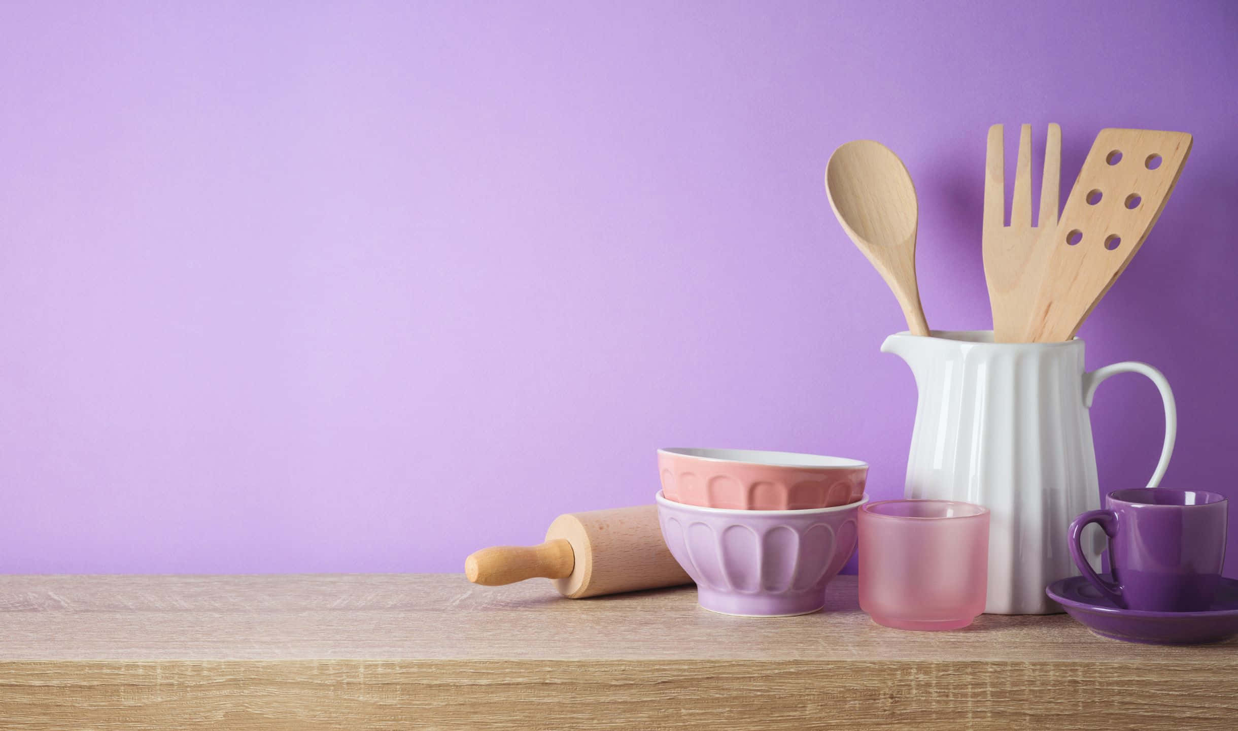 kitchen 桌布 壁紙 — 柔和紫色牆壁背景下，木製檯面上擺放著包括碗、擀麵棍和木製器具在內的粉彩廚房用具。