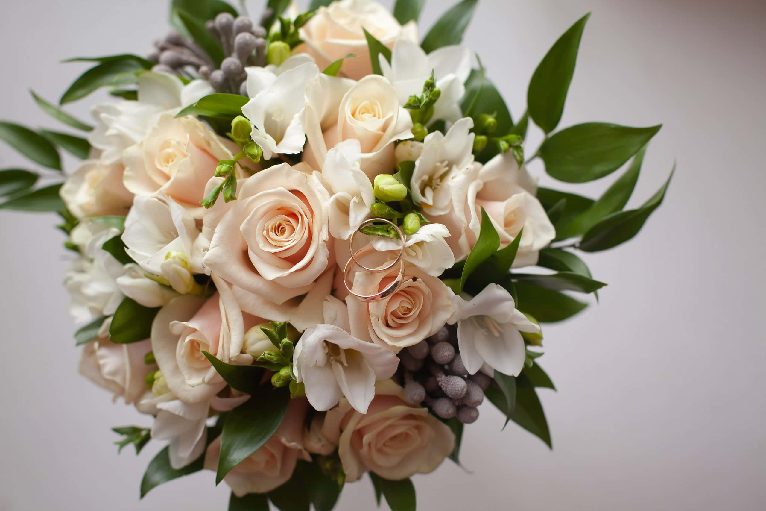 Wedding Bouquet 桌布 壁紙 — 柔和蜜桃色與白色新娘花束，搭配綠葉，兩枚金色結婚戒指藏於花朵之間。
