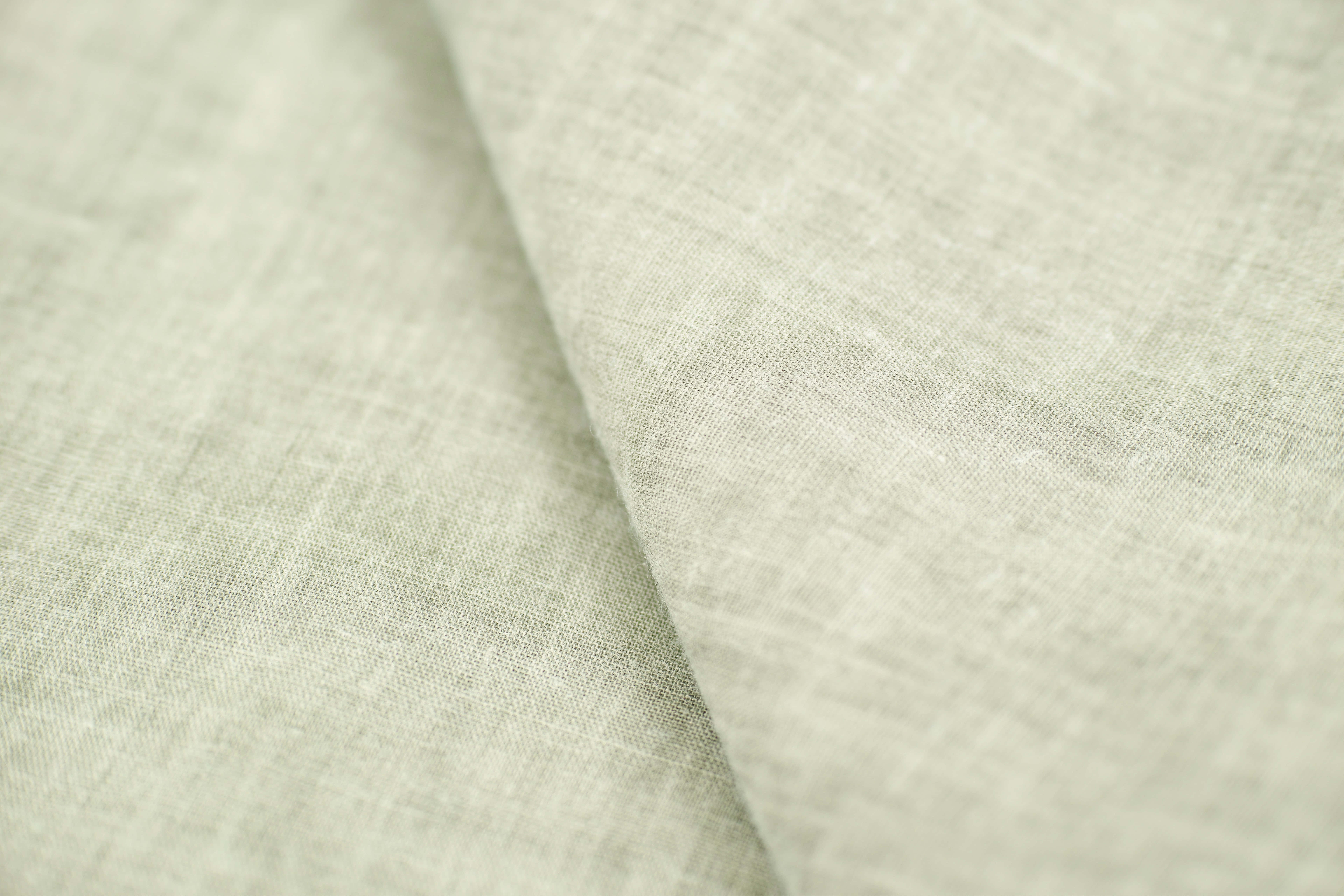 Textured 桌布 壁紙 — 柔軟淺綠色亞麻布料的特寫，具有天然編織紋理和柔和摺痕。