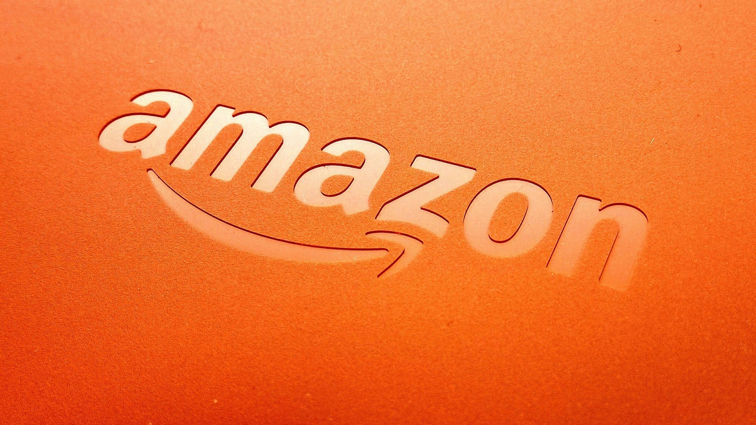 亞馬遜 桌布 壁紙 — 柔軟燈光下，紋理橙色材質上壓印的Amazon標誌特寫。