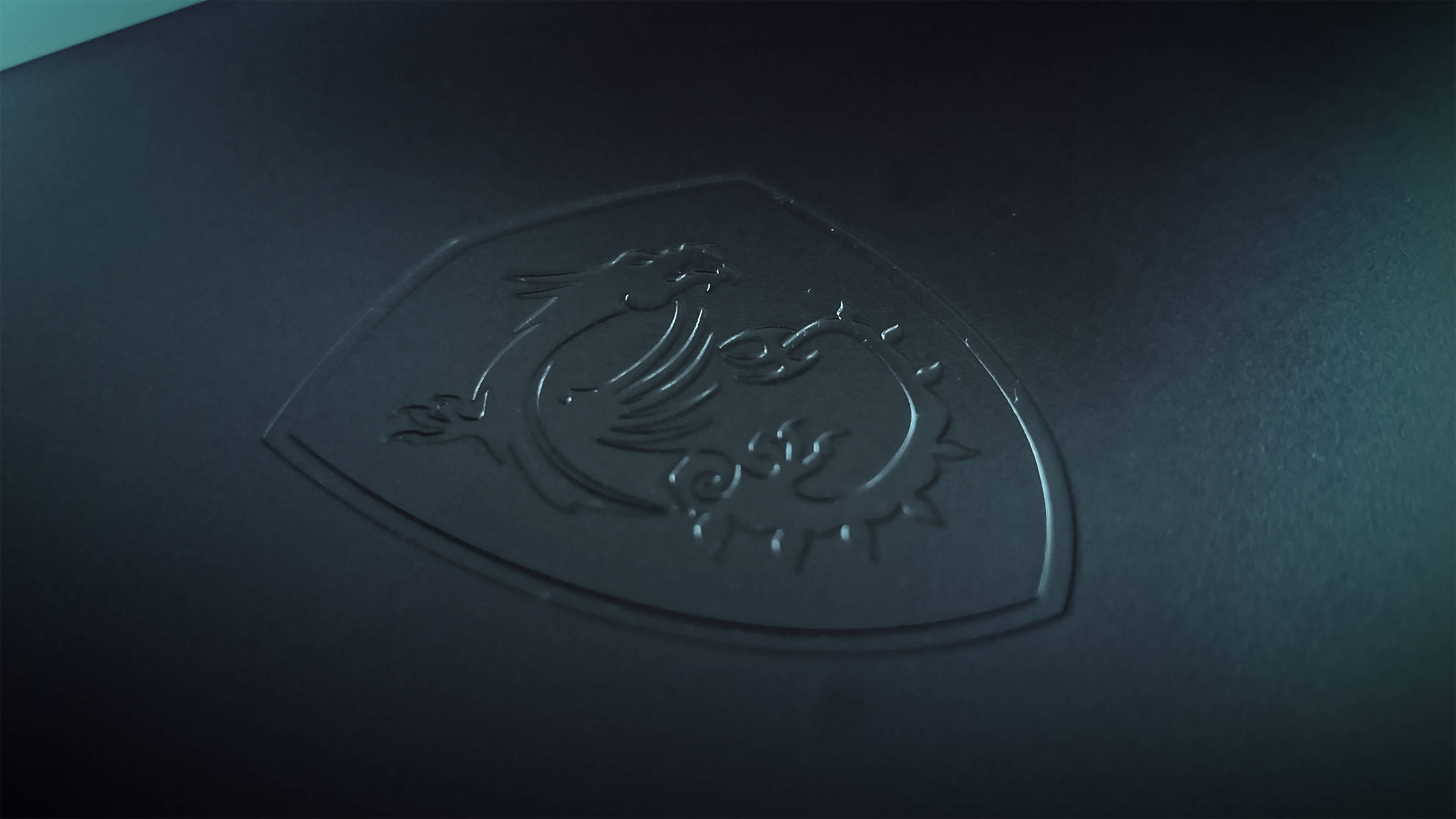msi 2560x1080 桌布 壁紙 — 柔軟燈光下，霧面表面上壓印的時尚黑色MSI龍標誌特寫。