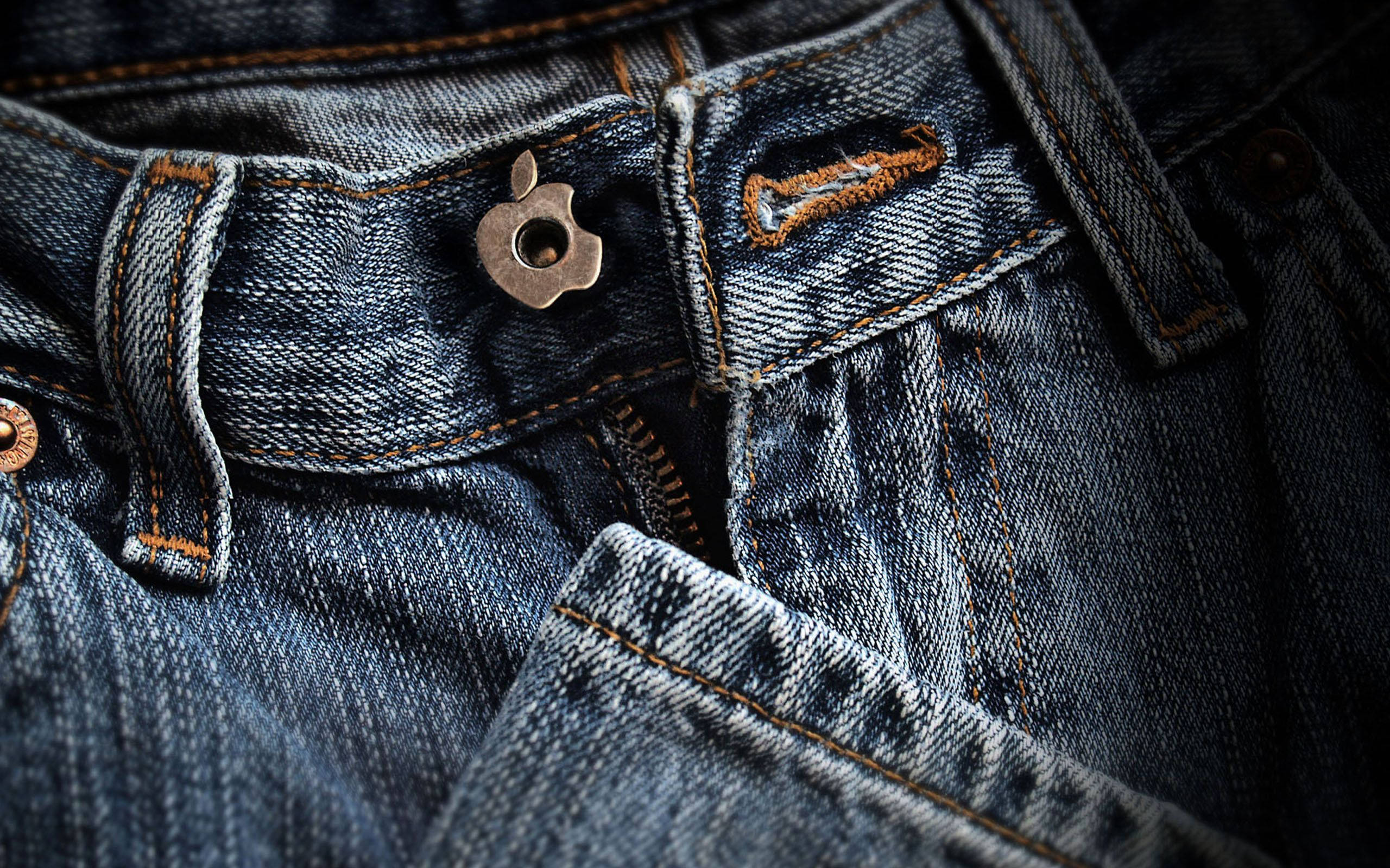 Denim 桌布 壁紙 — 柔軟燈光下磨損的牛仔褲特寫，帶有金屬蘋果鈕扣和橙色縫線。