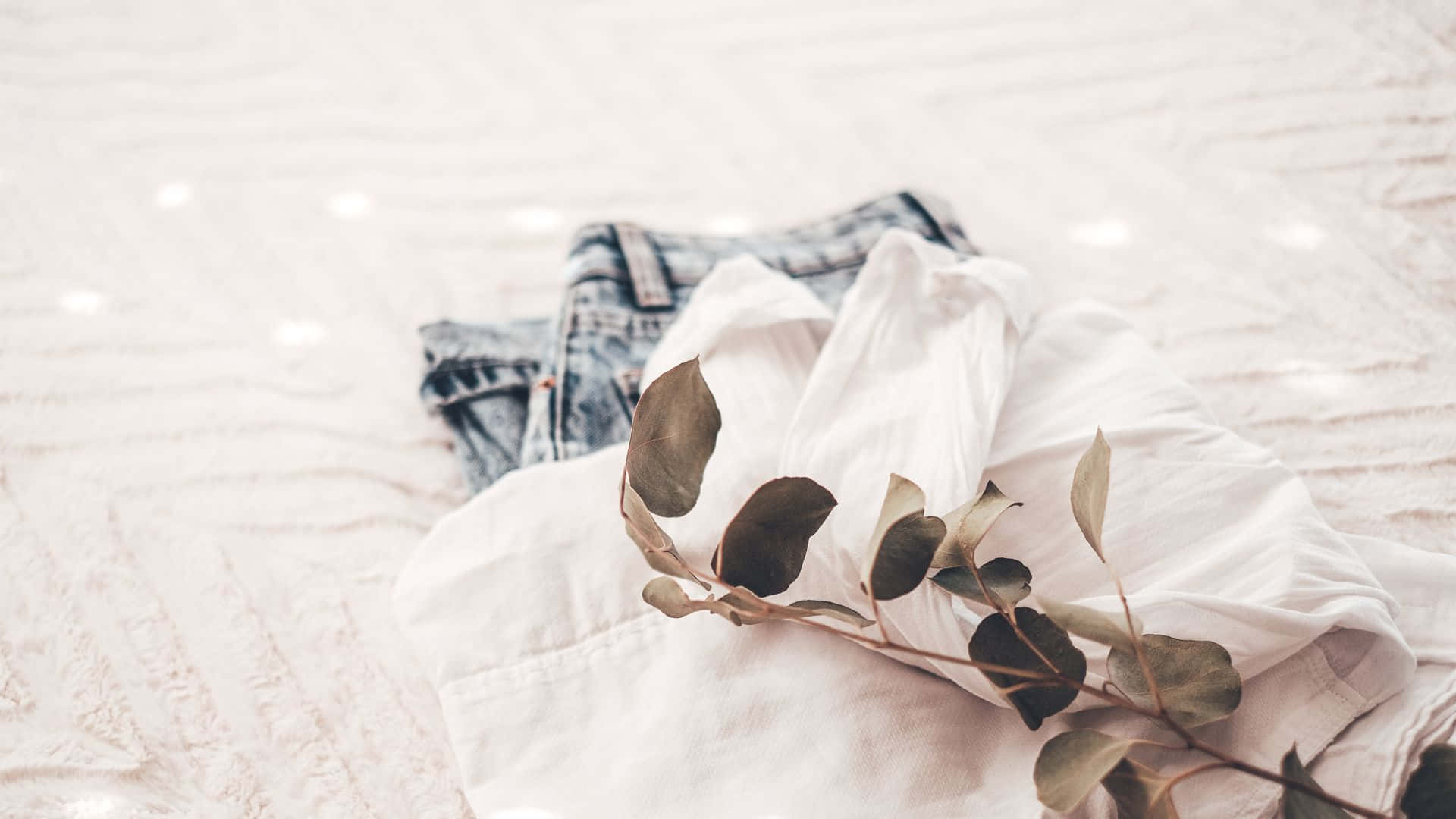 Jeans 桌布 壁紙 — 柔軟白色襯衫和牛仔褲放在帶有紋理的床罩上，尤加利樹枝增添自然優雅。