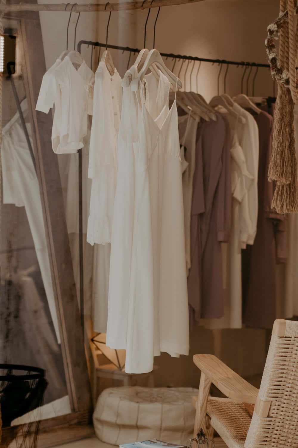 Clothes 桌布 壁紙 — 柔軟的白色和淡紫色衣物整齊地掛在一個質樸的金屬架上，店內燈光溫暖，配有藤編家具。