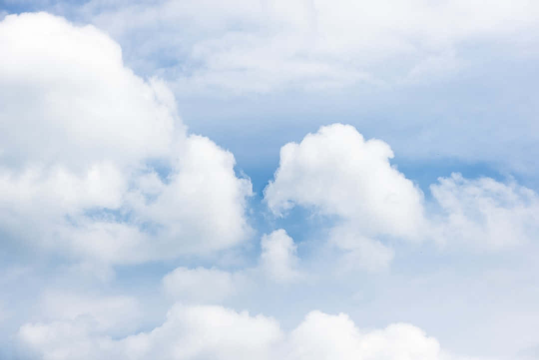 Blue Skies 桌布 壁紙 — 柔軟的白雲在晴朗的藍天上慵懶地飄動，構成寧靜的日間景象。