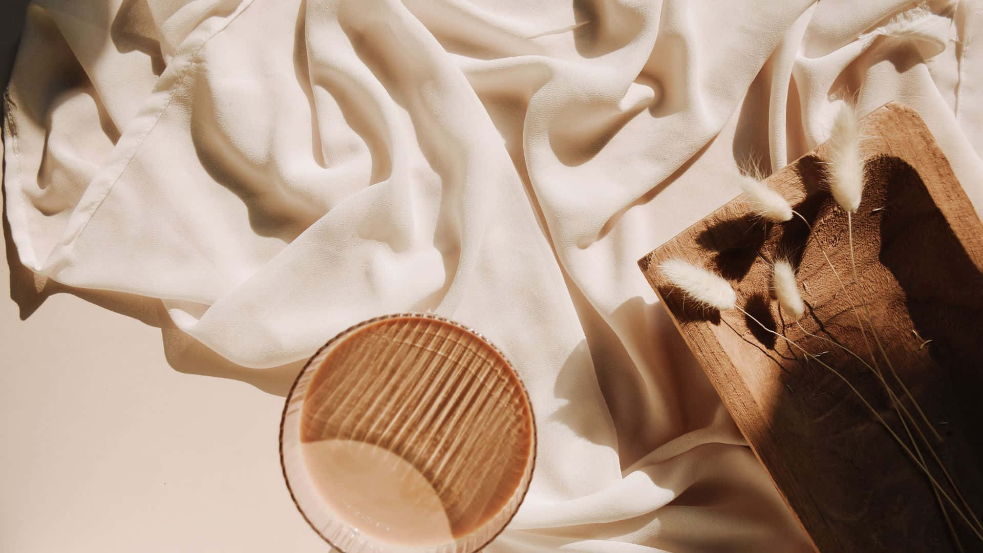 Brown Pastel Aesthetic 桌布 壁紙 — 柔軟的米色布料在溫暖的陽光下垂墜在一個木碗和一個盛有蓬鬆乾草的木托盤周圍。