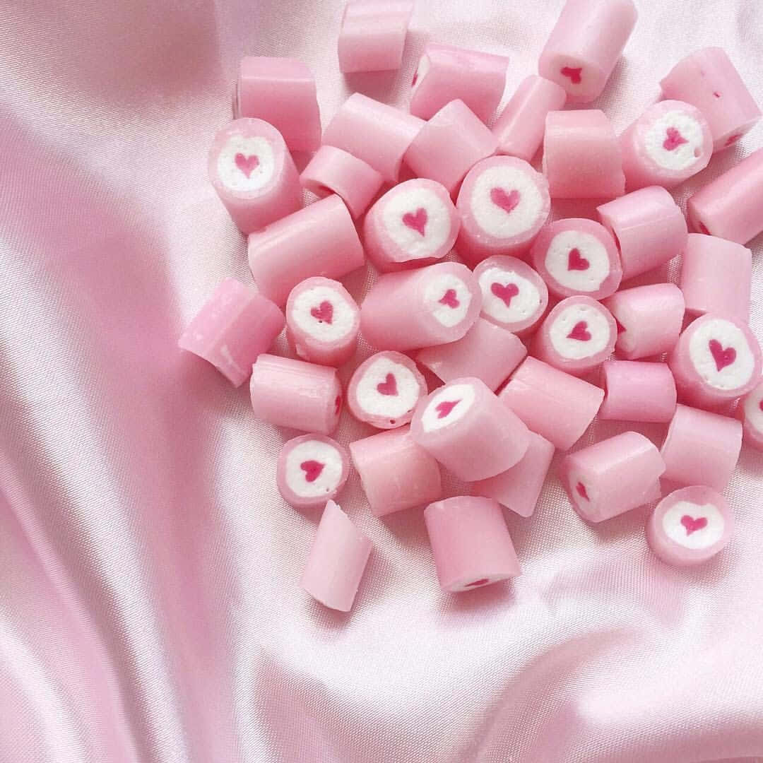 Pastel Pink Aesthetic 桌布 壁紙 — 柔軟的粉紅色心形糖果散落在絲滑的粉紅色布料上，形成甜蜜浪漫的佈置。