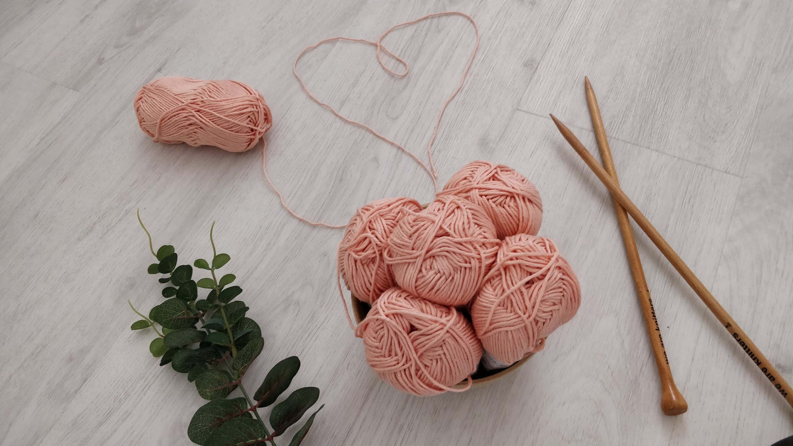 Knitting 桌布 壁紙 — 柔軟的粉紅色毛線球放在碗裡，配上編織針和綠色植物，置於淺色木地板上。