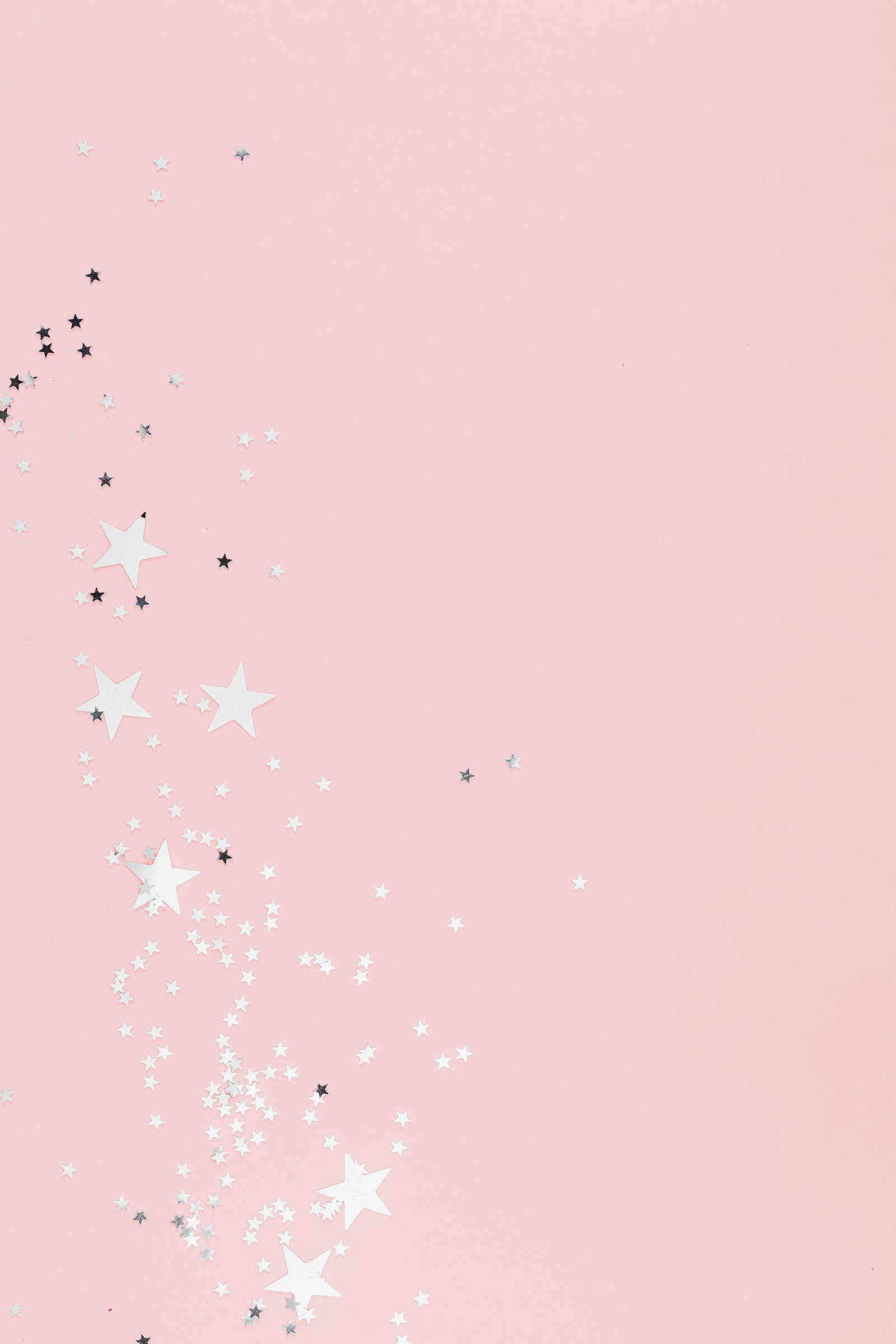 Pastel Pink Aesthetic 桌布 壁紙 — 柔軟的粉紅色背景，點綴著散落的白色和銀色星星形狀的紙屑，營造出一個奇幻的天體效果。